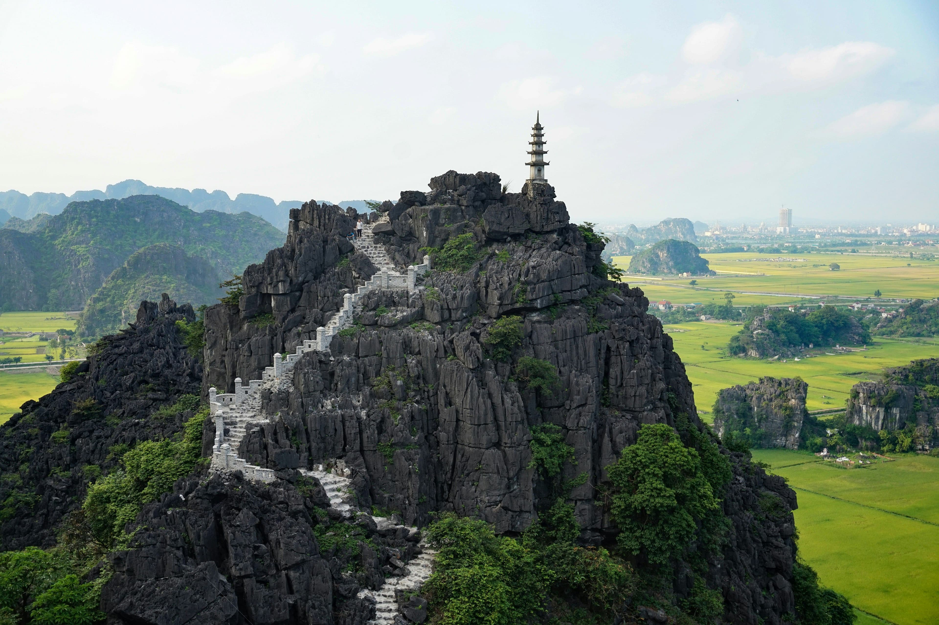 A rock with stairs going up the mountain in Ninh Binh surrounded by rivers