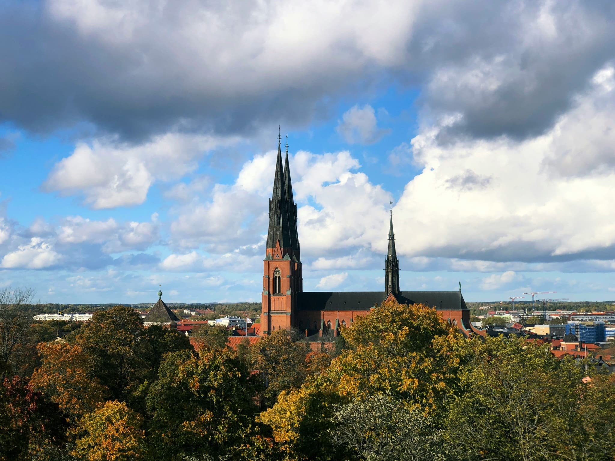 Uppsala Cathedral surrounded by green trees and clouds
