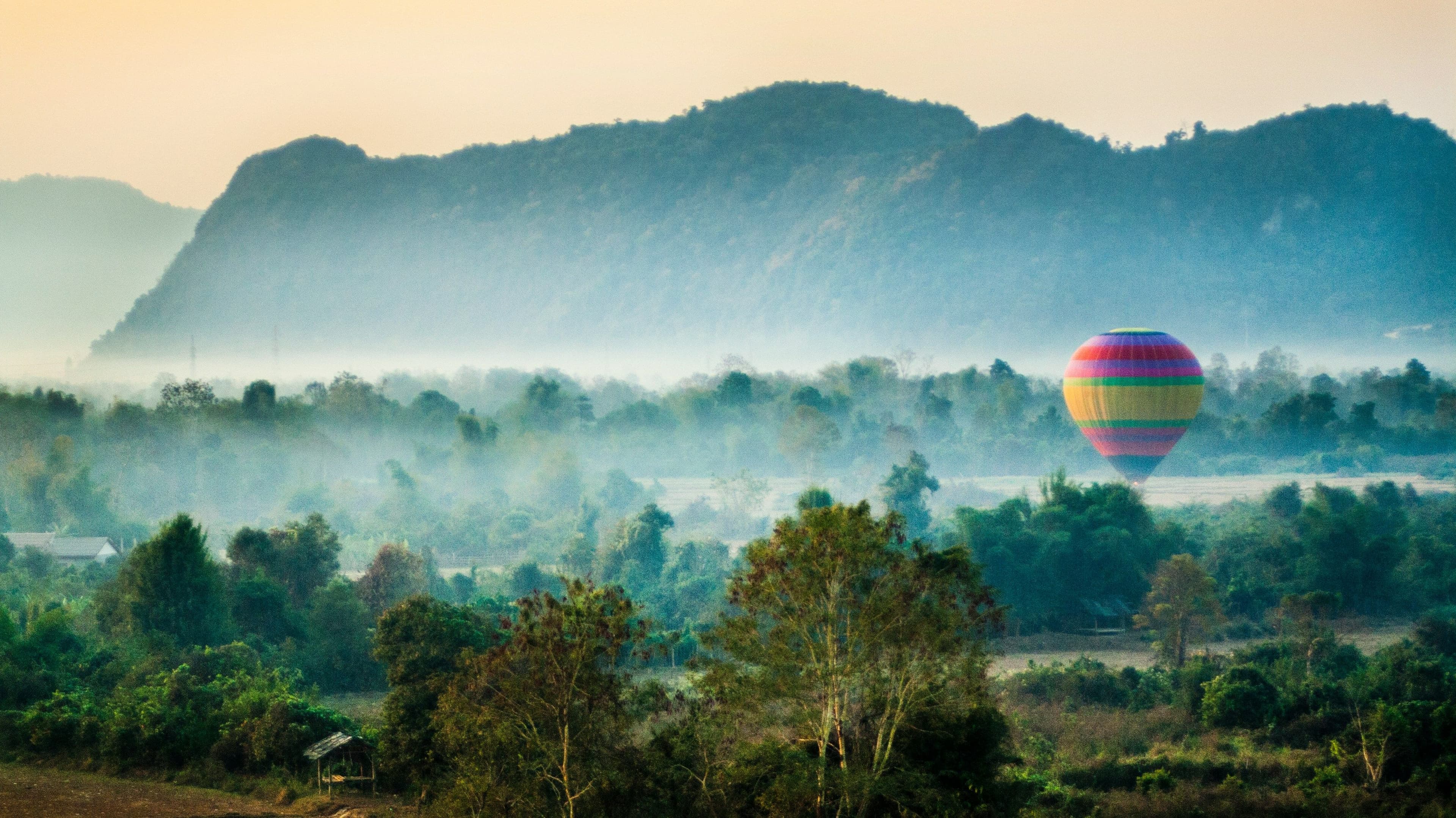 Misty landscape with mountains and a hot air balloon on the right.