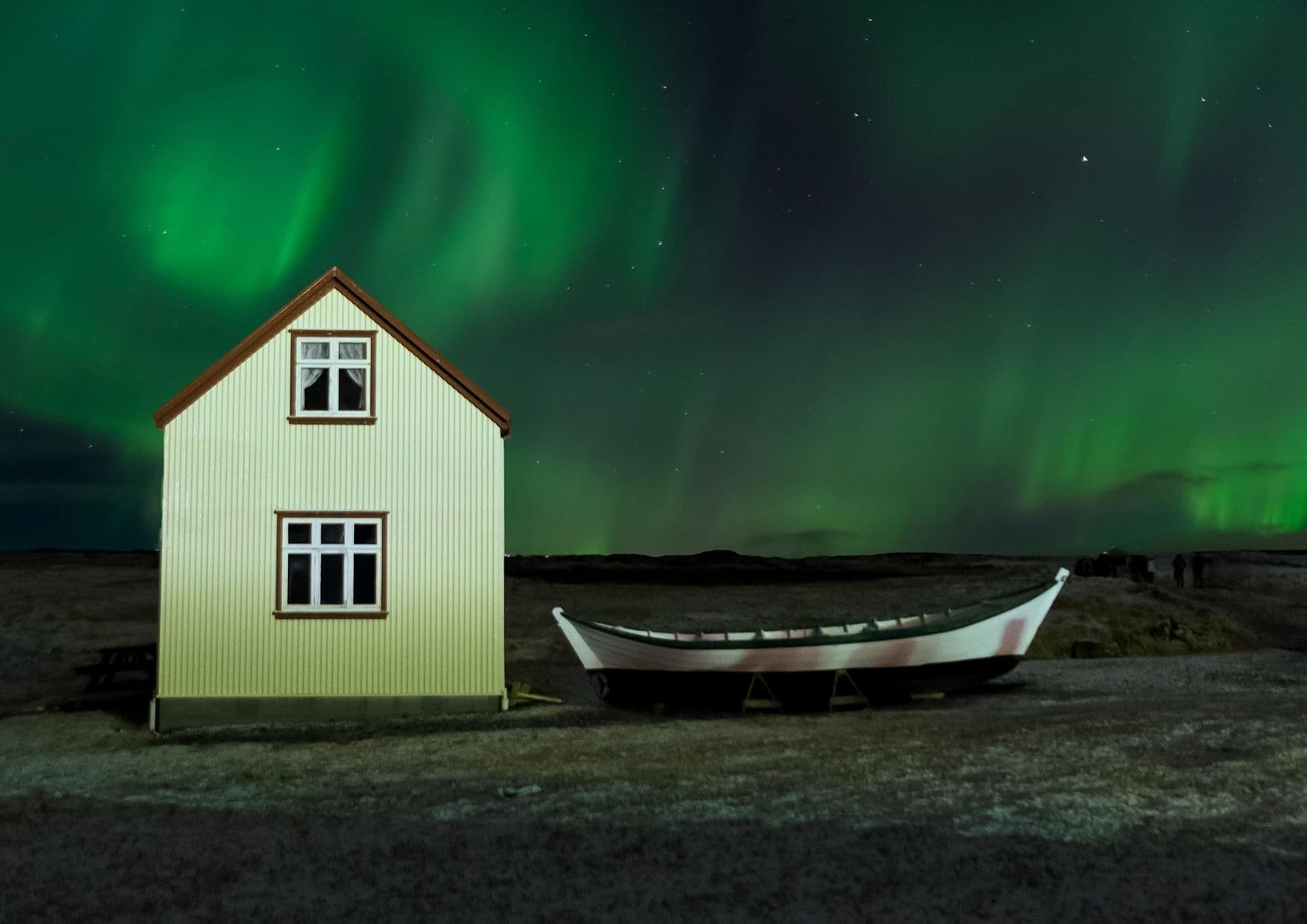 Northern lights reflected over small white house and boat in Iceland
