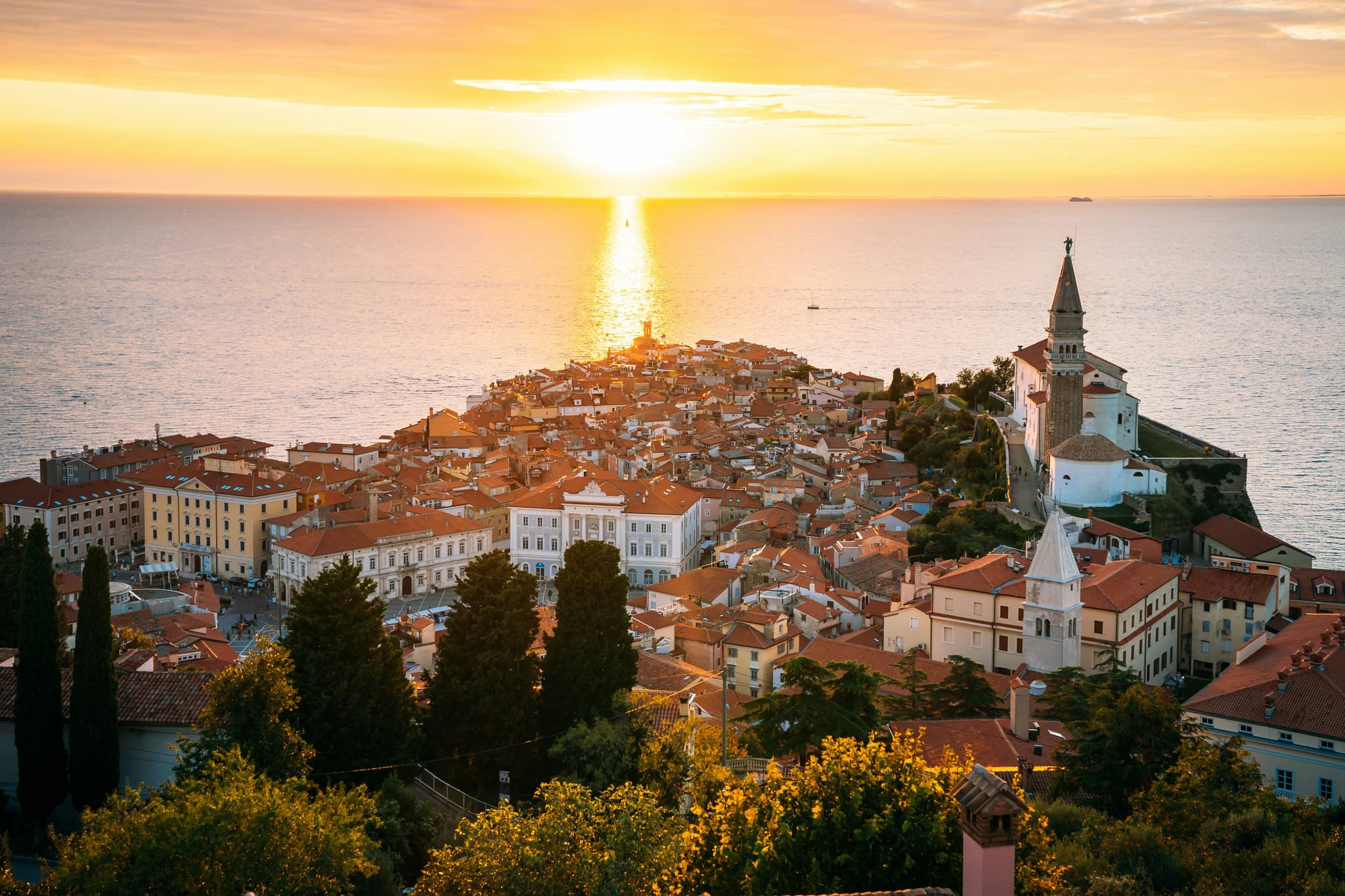 Sunset view of Piran, a city with colorful houses and a castle overlooking the ocean