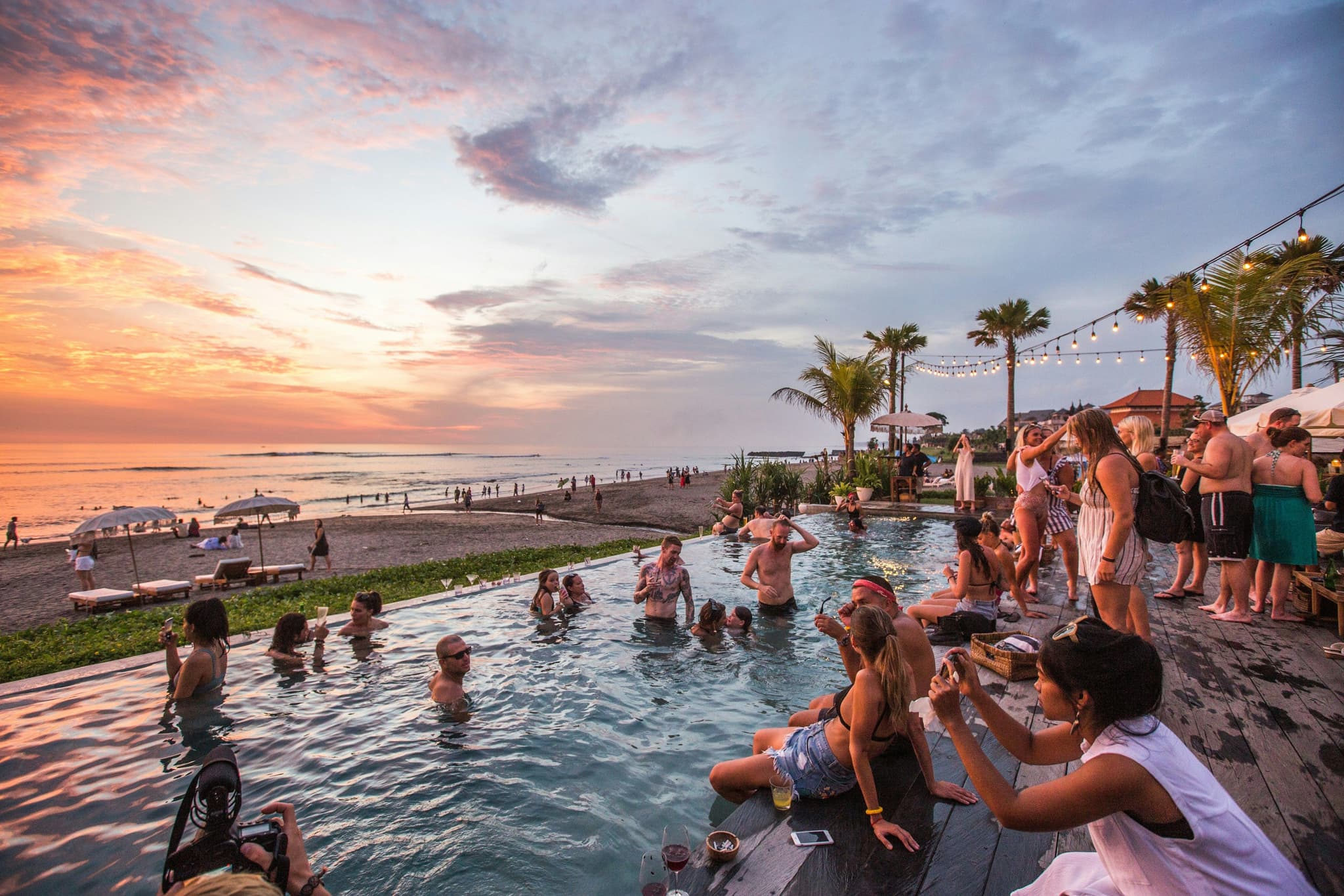 Many travellers standing and sitting by the pool at sunset in Bali
