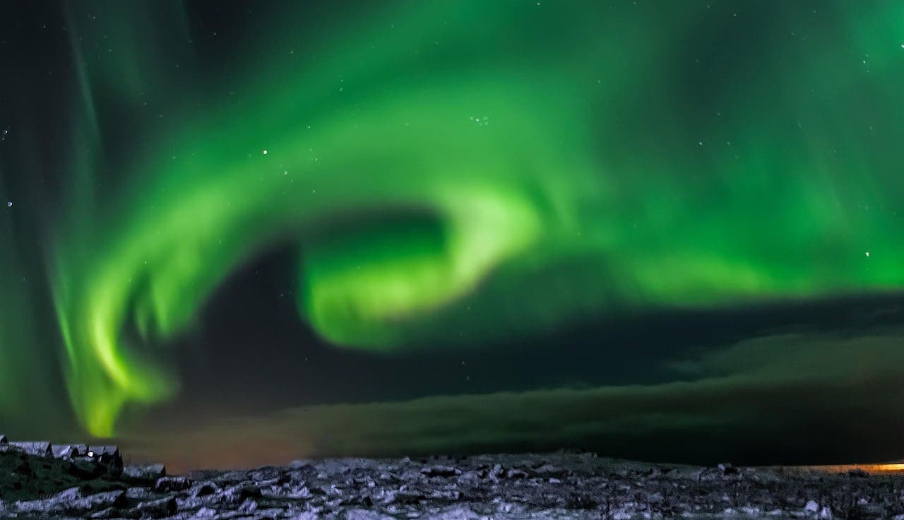 Northern lights glowing bright green above a rocky Icelandic coastline at night.