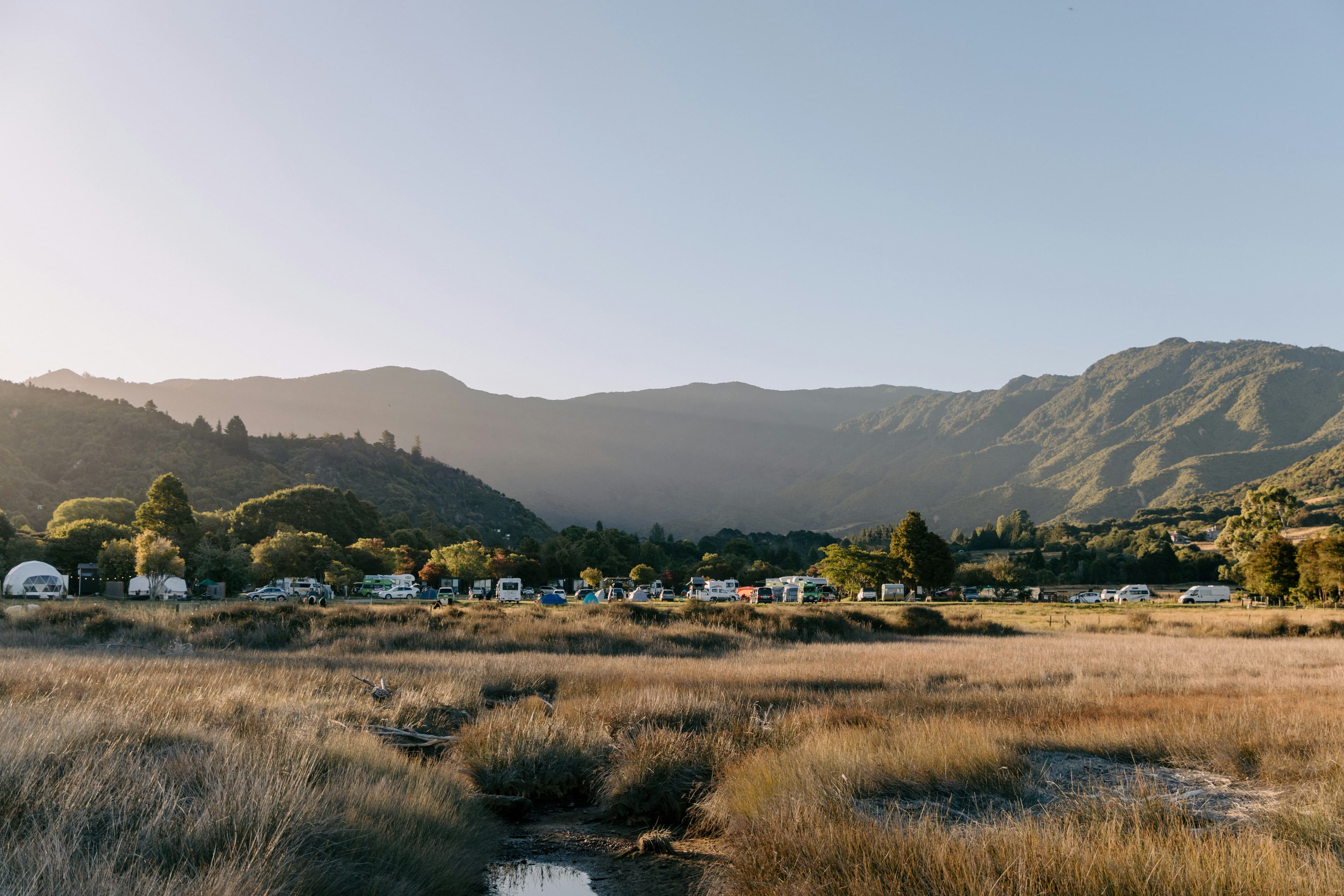 Orange grass field in Abel Tasman National Park surrounded by mountains during sunrise