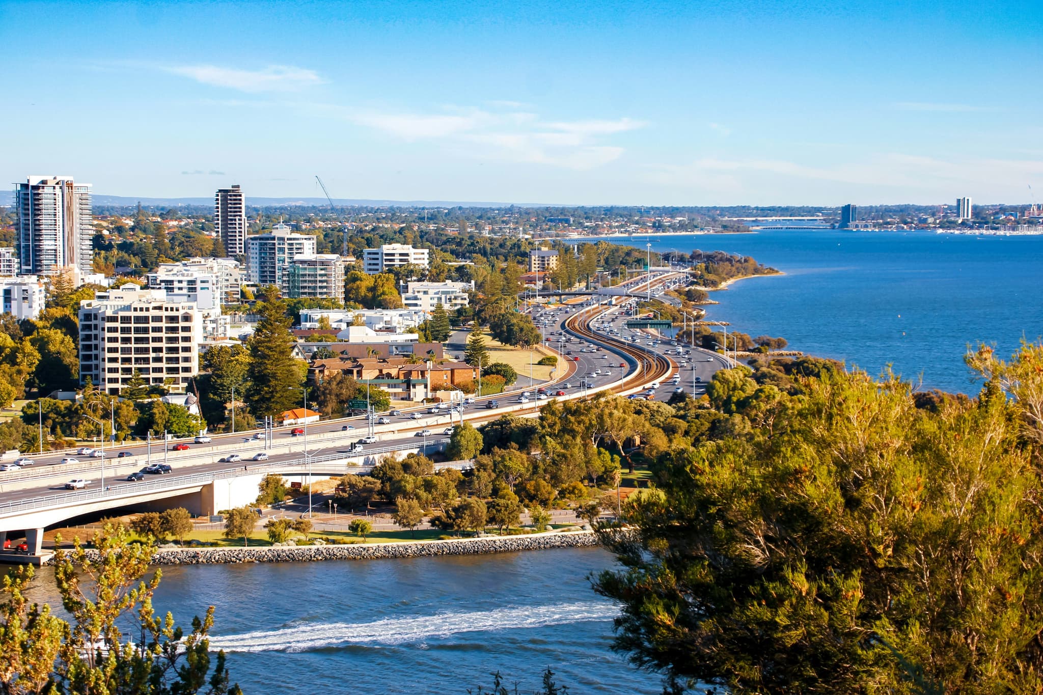 The city of perth from above, the ocean and city buildings visible along a road.