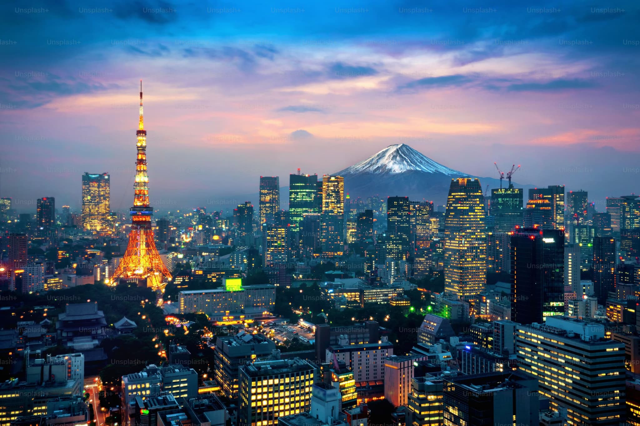 Cityscape of Tokyo at dusk, highlighting the illuminated Tokyo Tower amidst skyscrapers, with snow-capped Mount Fuji in the background under a colorful sky.