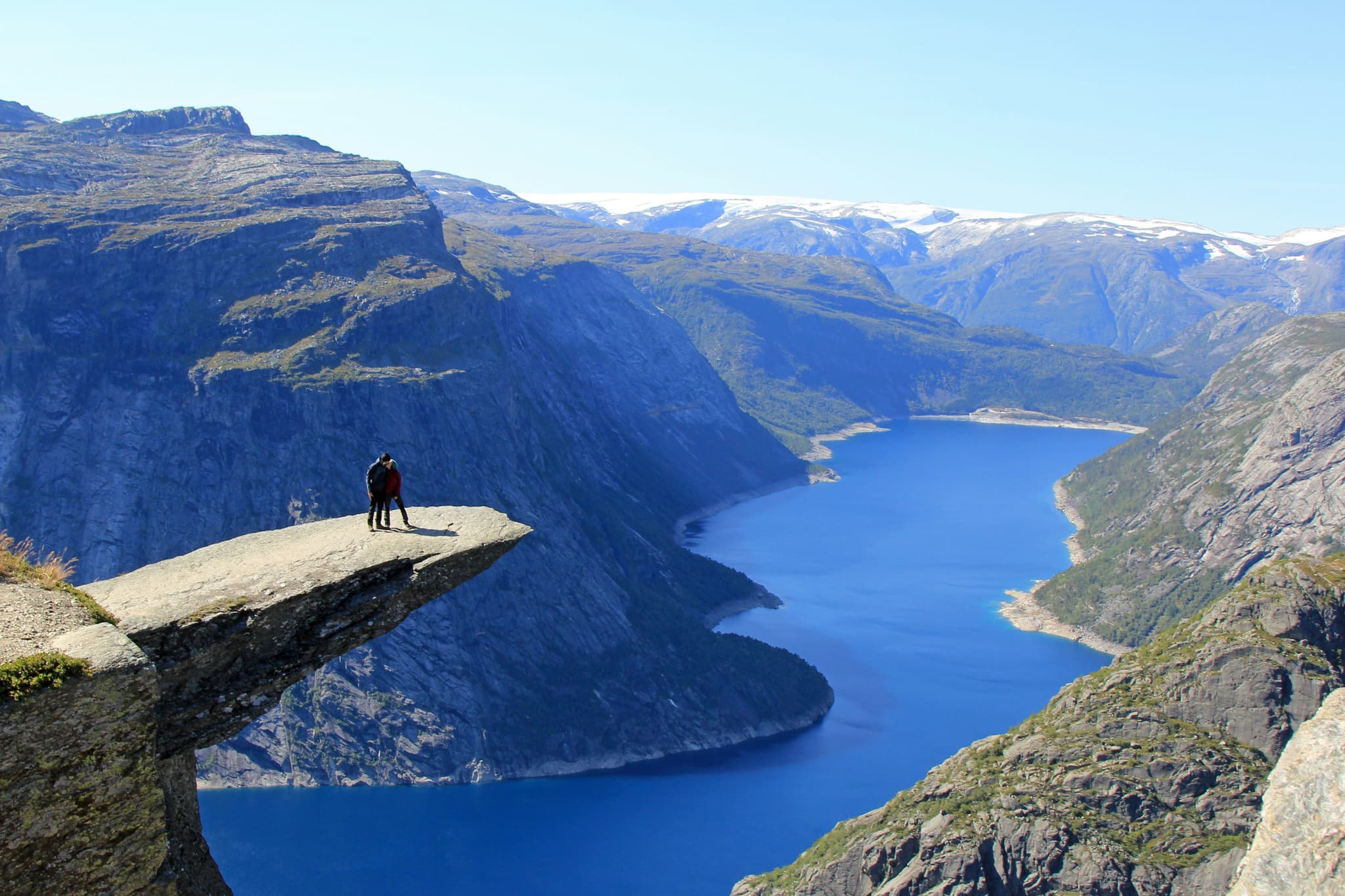 Two people standing on the edge of a cliff surrounded by river and moutains in Trolltunga