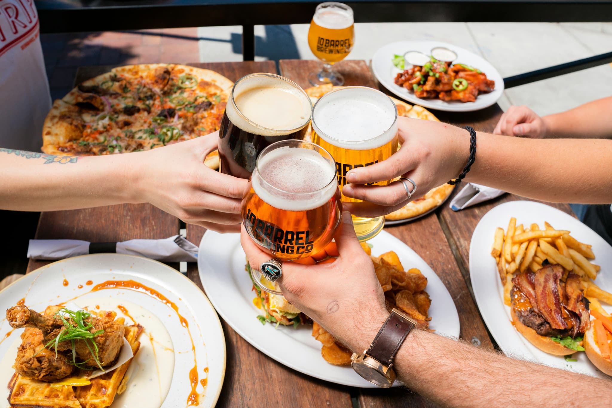 Hands of people holding beers in beer garden with pitta and fried on their plates