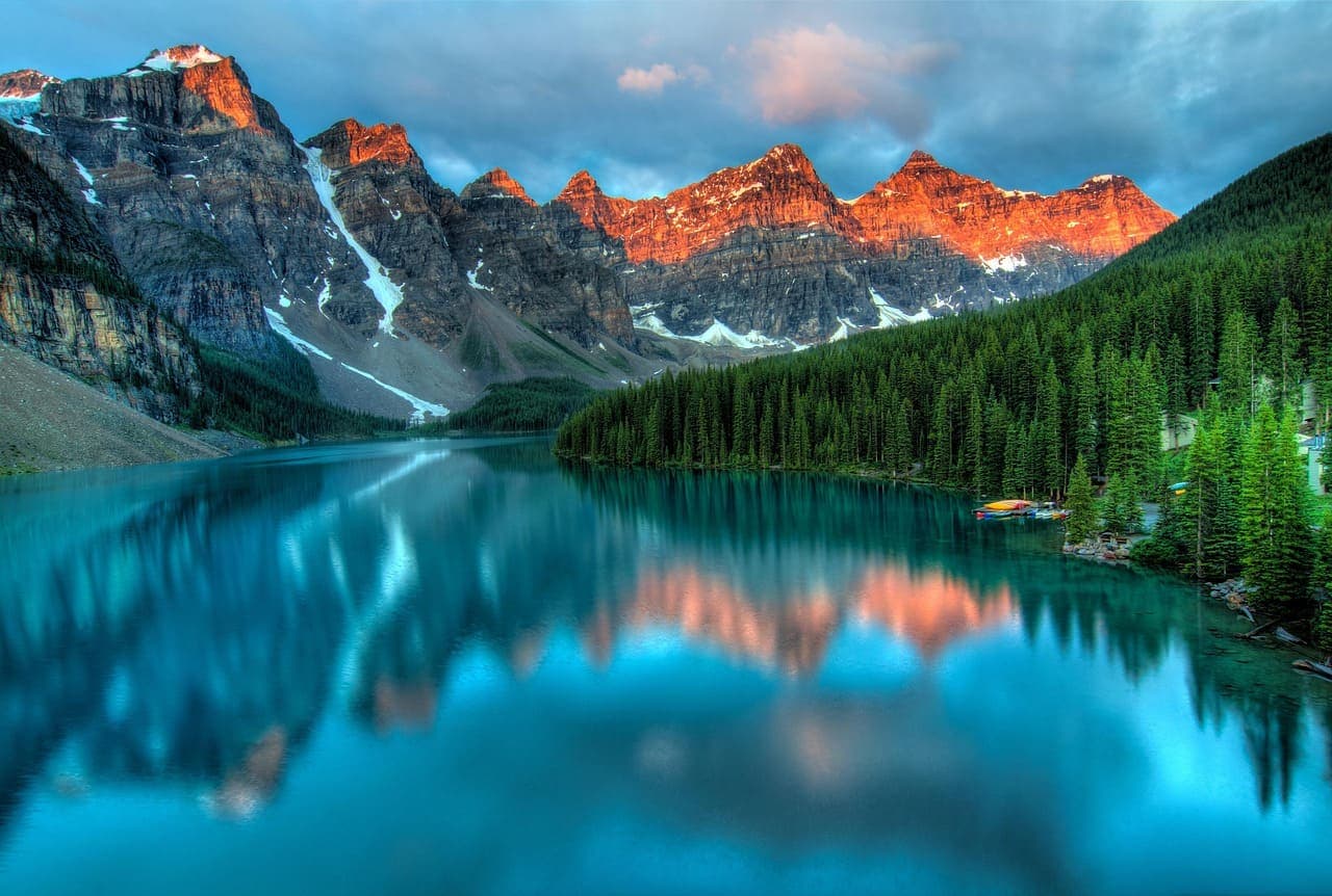 Turquoise lake in the Canadian Rockies surrounded by pine forests and high mountain peaks reflecting in the calm water.