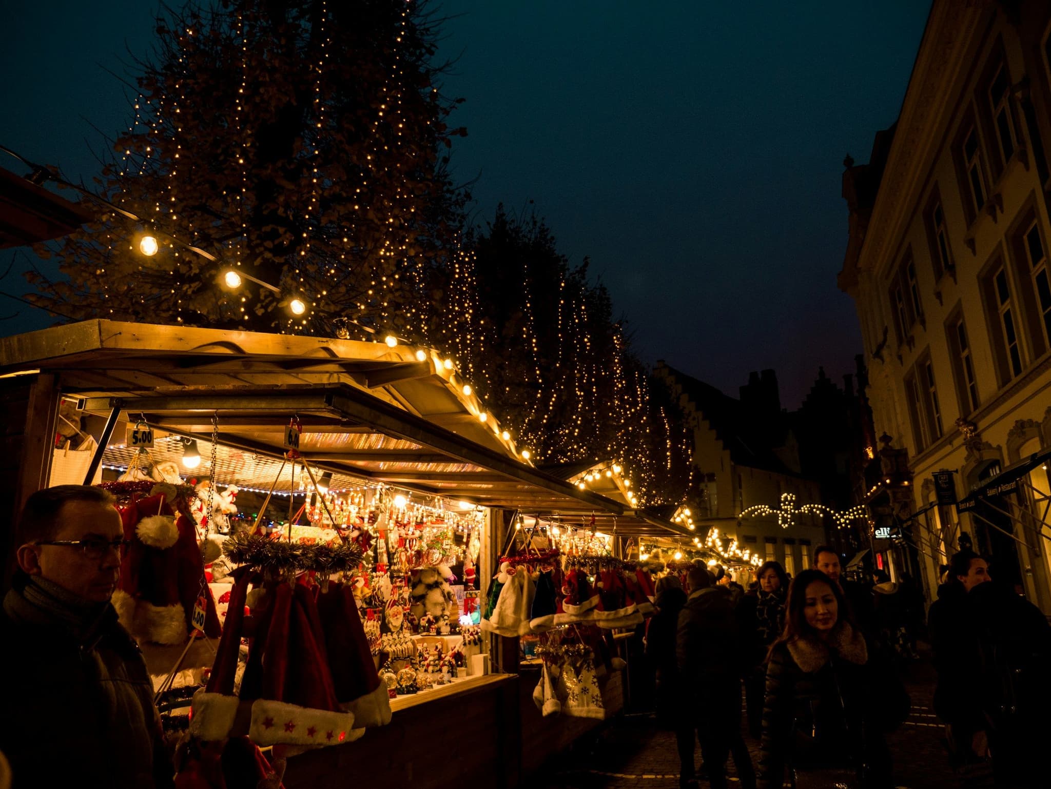 People walking past Christmas stalls at the market in Bruges at night