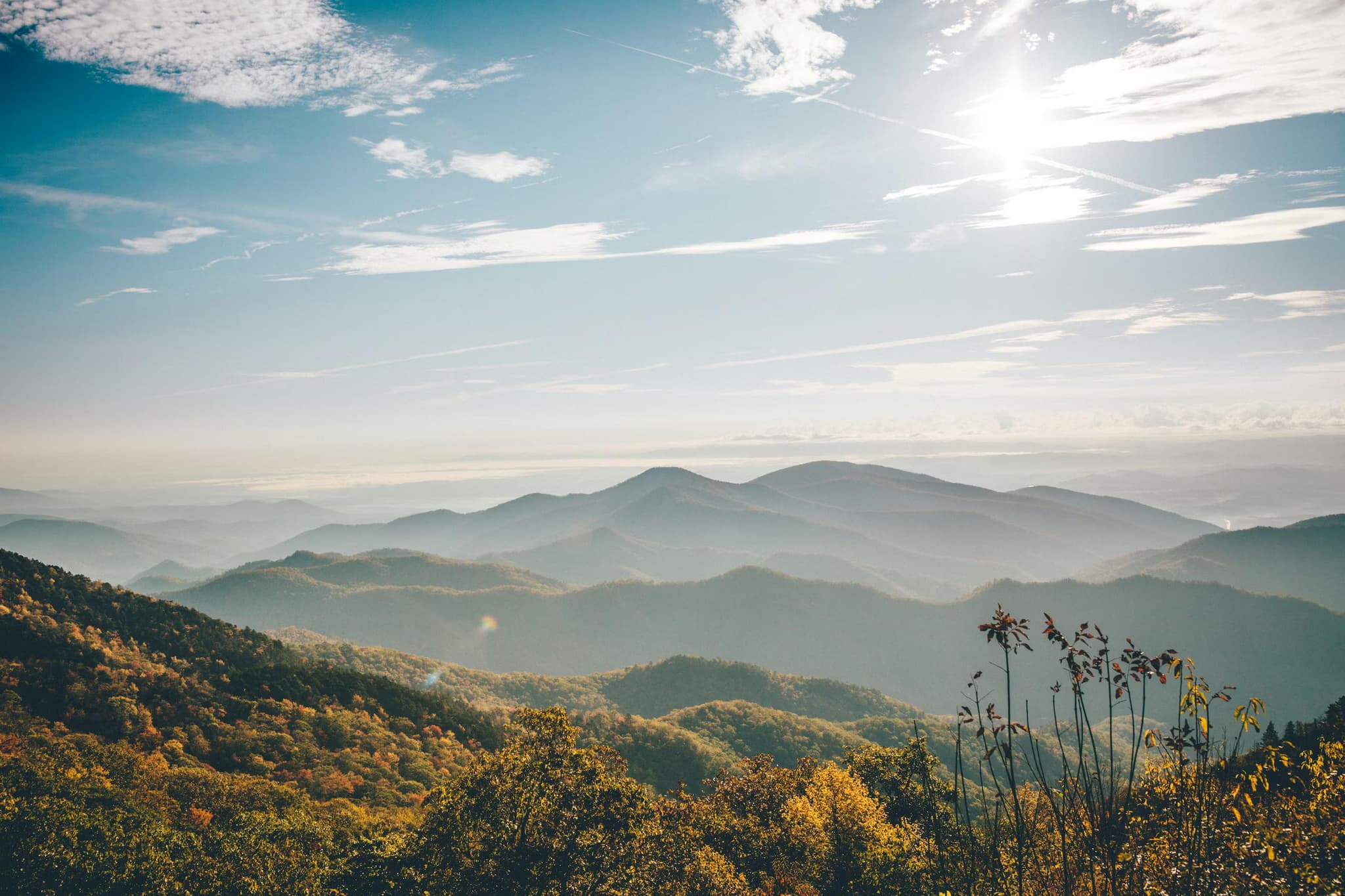 Dramatic landscape of rolling green hills and rugged cliffs under a cloudy sky, with a distant lake and mountains, conveying a sense of vastness and tranquility.