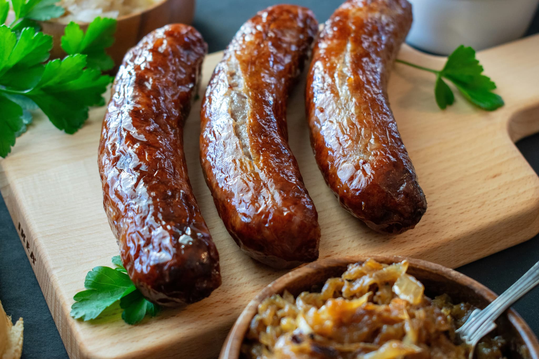 Three bratwurst on a wooden cutting board