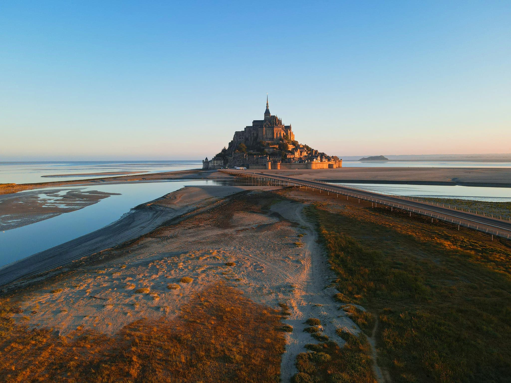 Mont Saint-Michel abbey surrounded by sand and tidal water during sunset