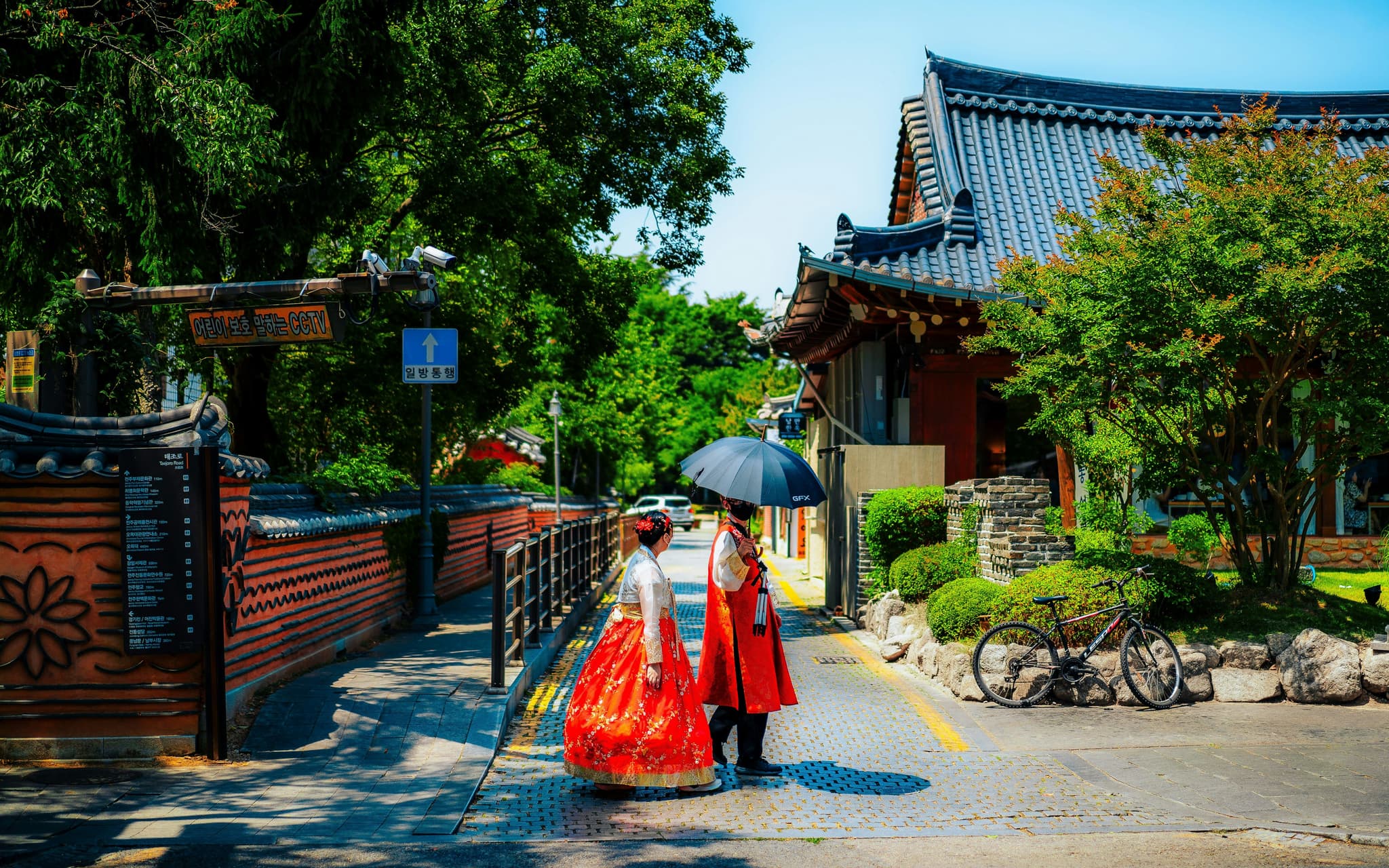 Two people in traditional clothing with umbrella walk on a cobble stone street next to temples inJeonju