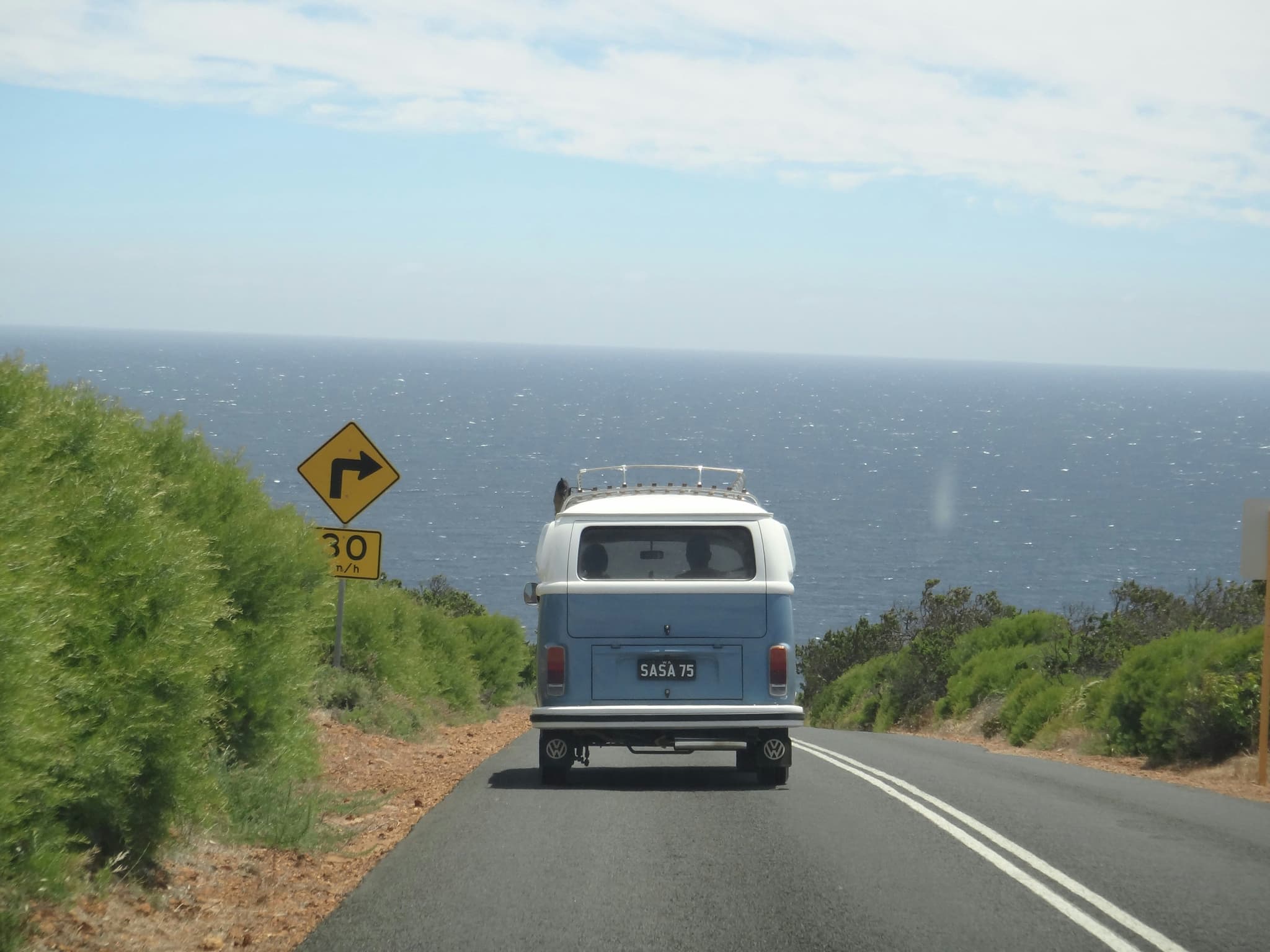 A campervan driving on the left side of the road on its way to the beach which is visible in the background