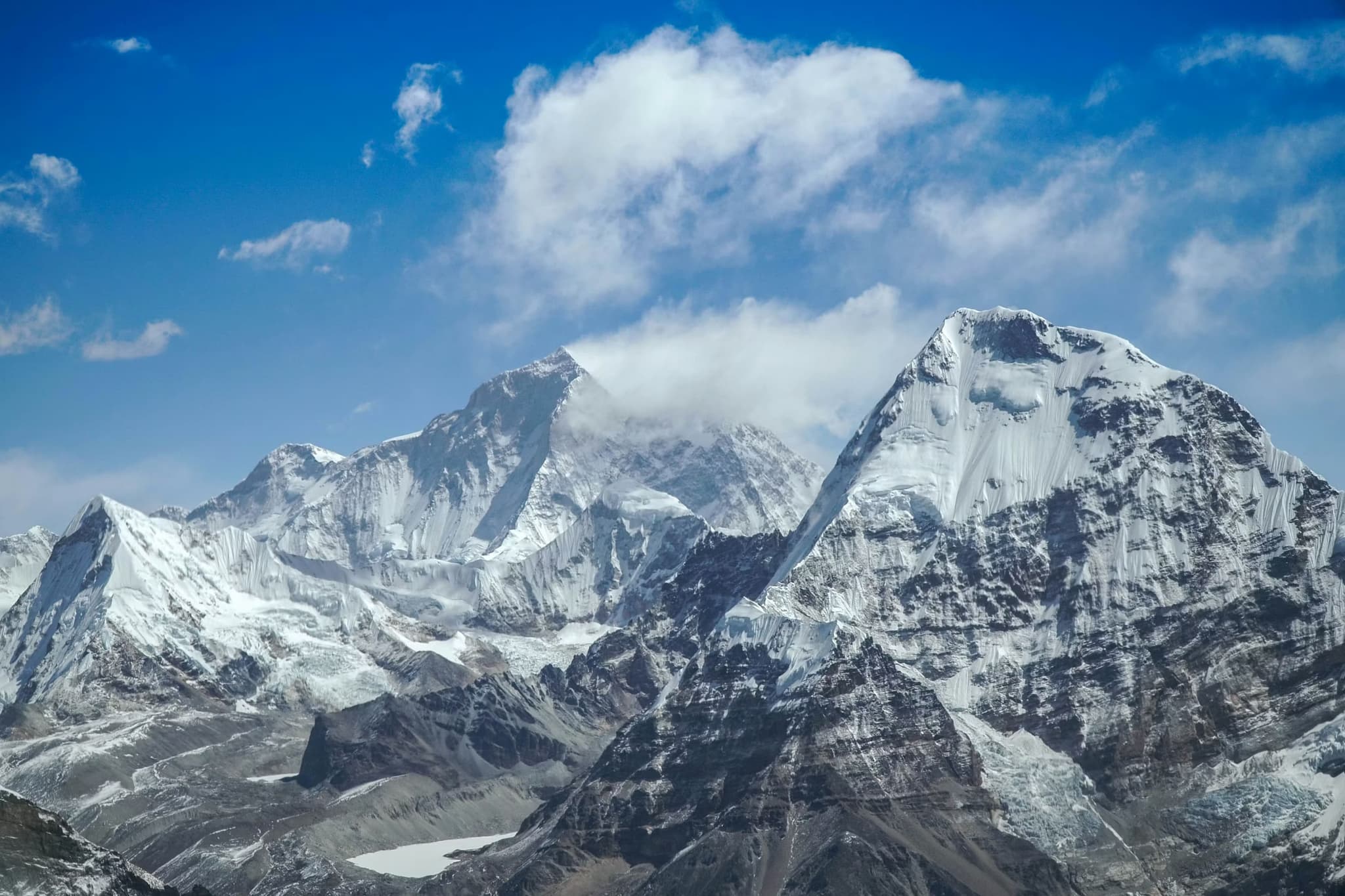 Snow-covered mountain peaks under a clear blue sky with scattered clouds, capturing a serene and majestic alpine landscape.