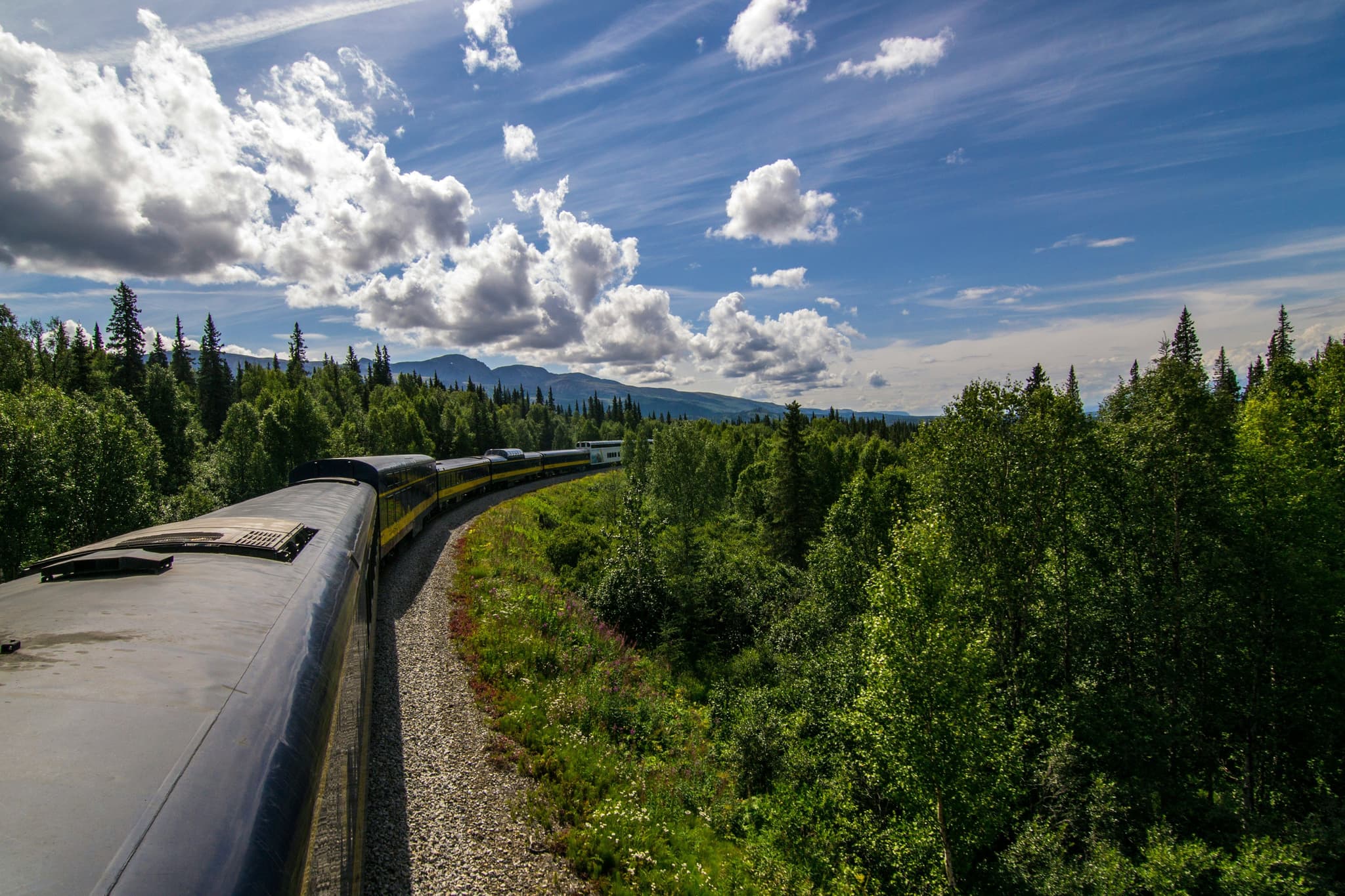 Top of a train riding through the forest mountains with clouds in the sky