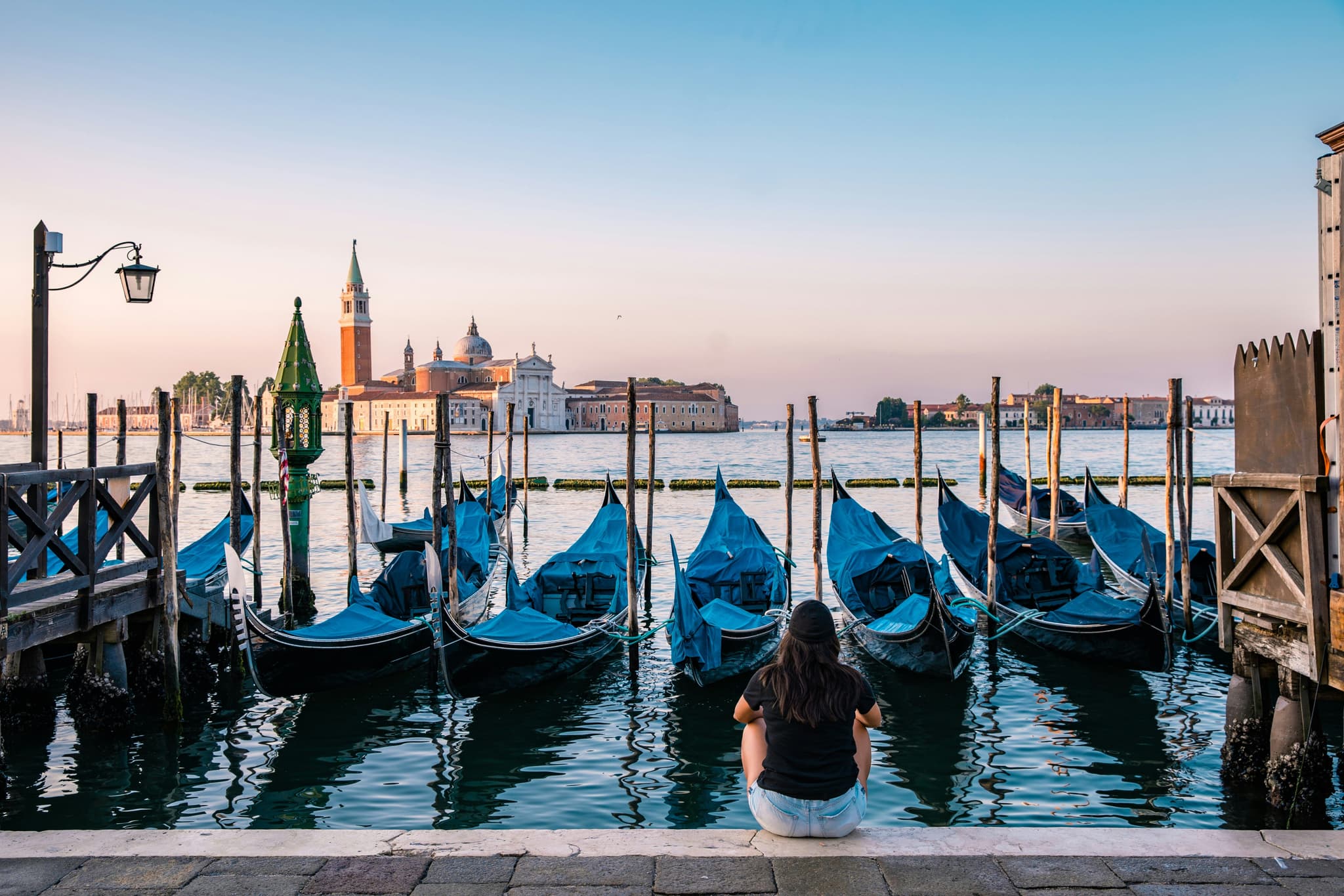 A woman sitting in front of gondolas in venice during sunset