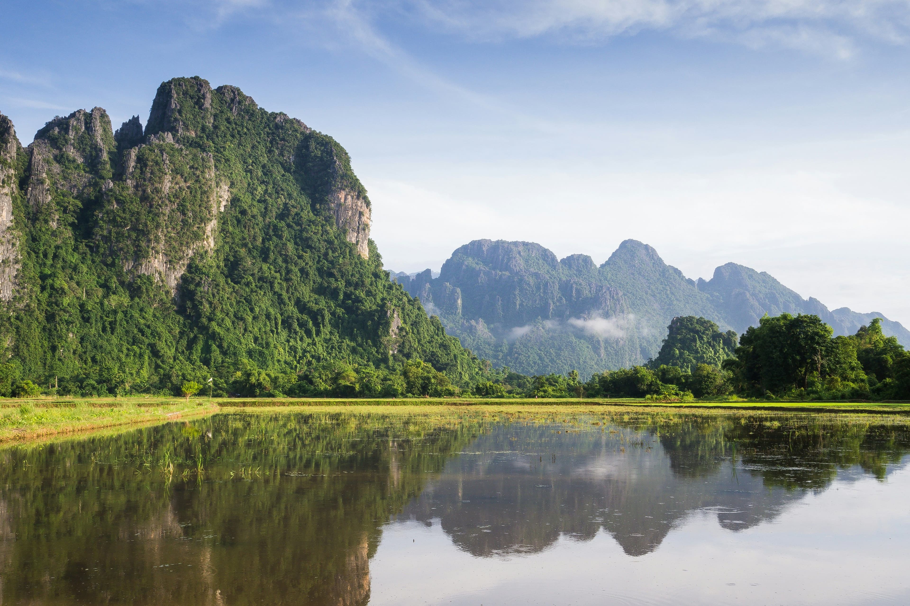 A scenic view of a lake and a limestone mountain peak behind it on a sunny day in Laos