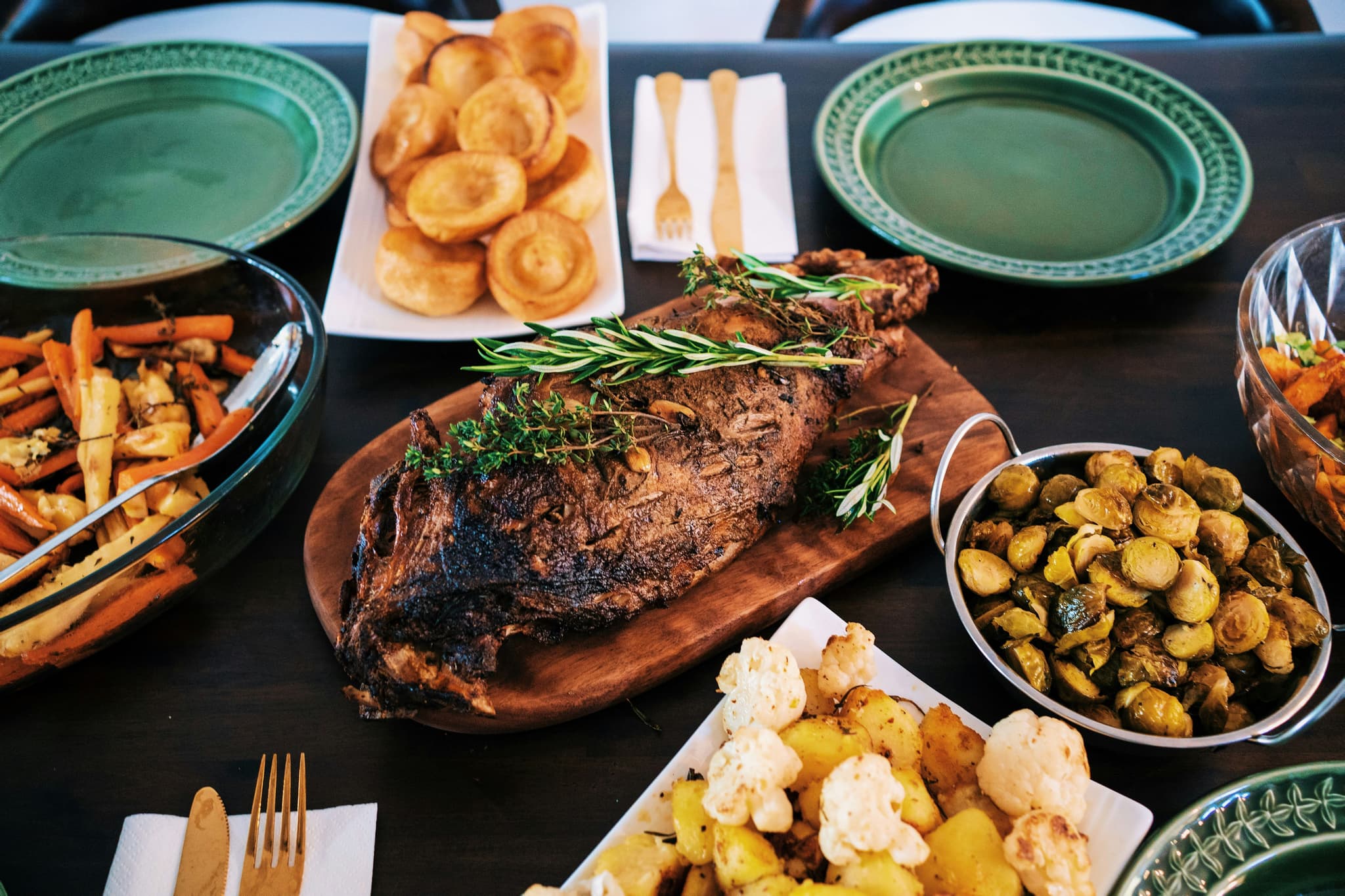 Sunday roast dinner, a big piece of meat in the middle of a table filled with dishes with potatoes and roast vegetables