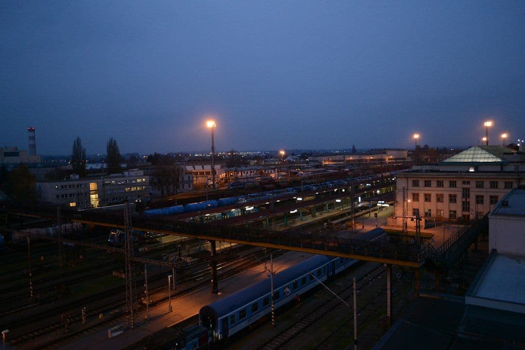A European train station lit up at dusk, tracks curving away into the evening.