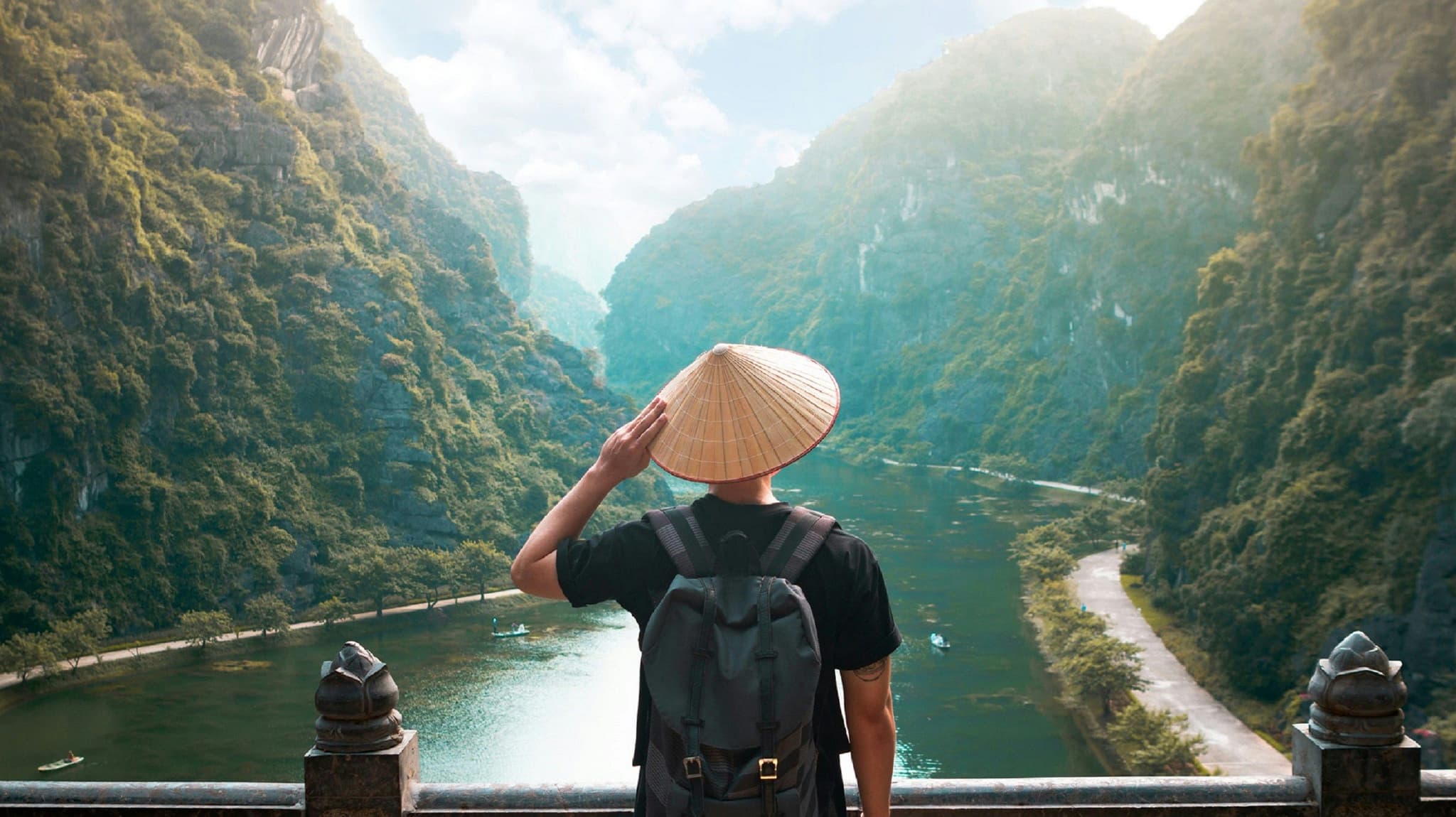 Tourist with Vietnamese hat overlooking a river surrounded by mountains in Vietnam