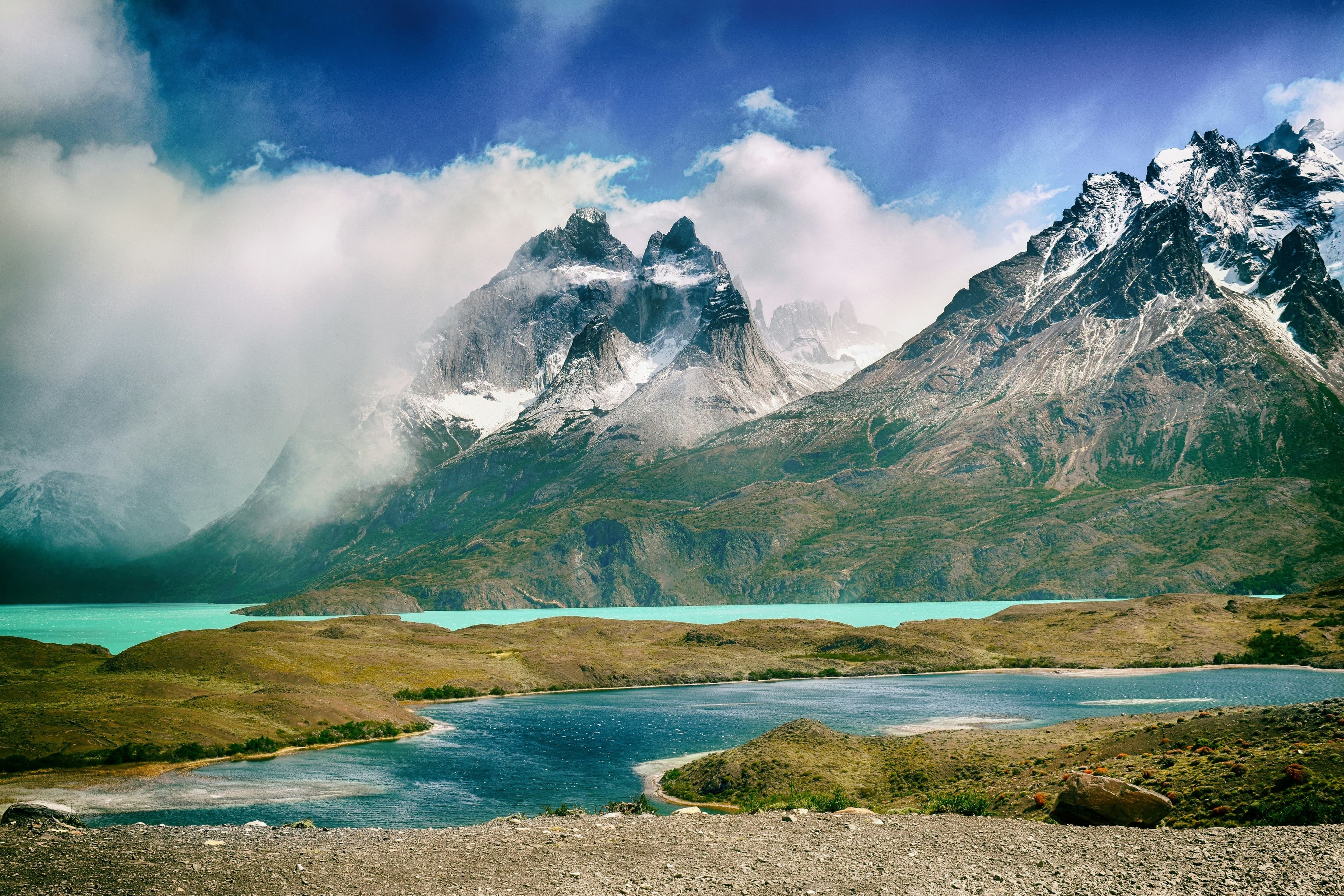 High mountain peaks with snow, clouds and a bright blue lake in Hike in Torres del Paine National Park