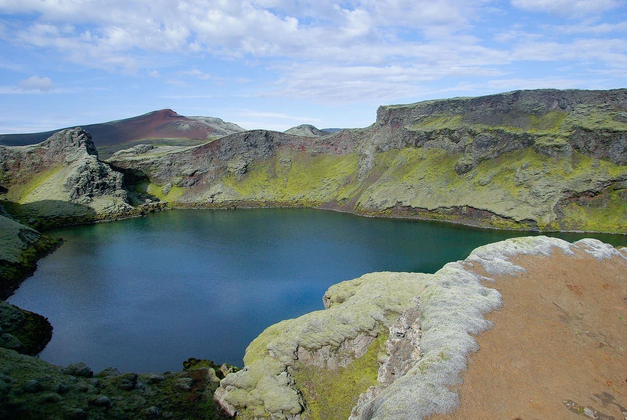 Volcanic crater lake near Lake Mývatn in North Iceland with green moss covered slopes and blue water.