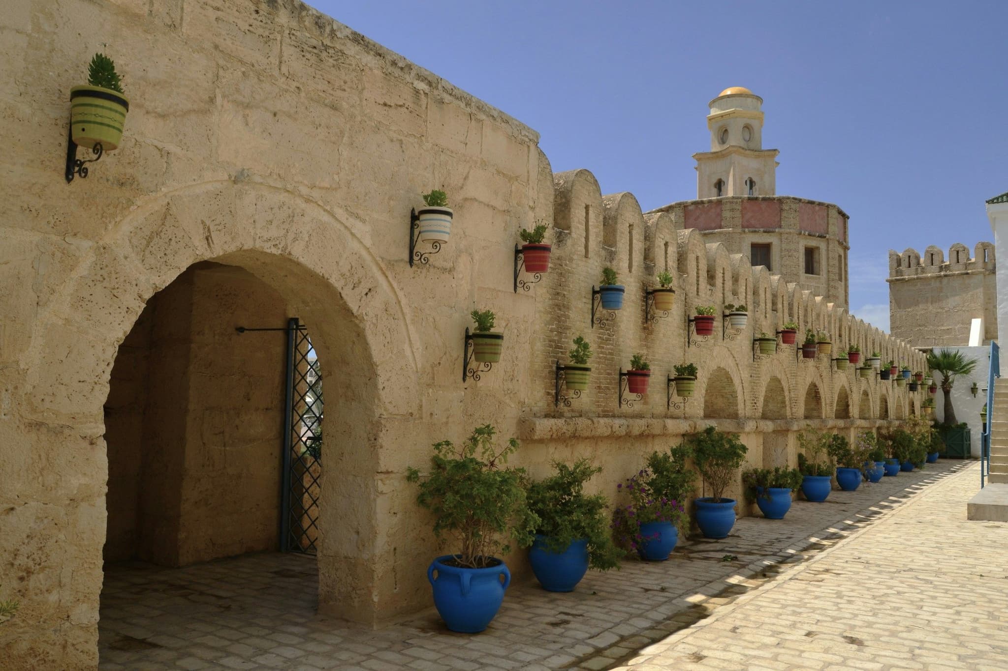 Crenellated walls, a stone gateway and blue planters at the medina in Yasmine Hammamet