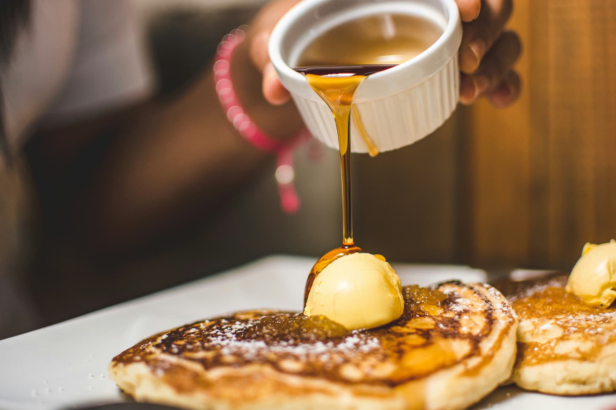 A hand pouring maple syrup on top of fluffy pancakes