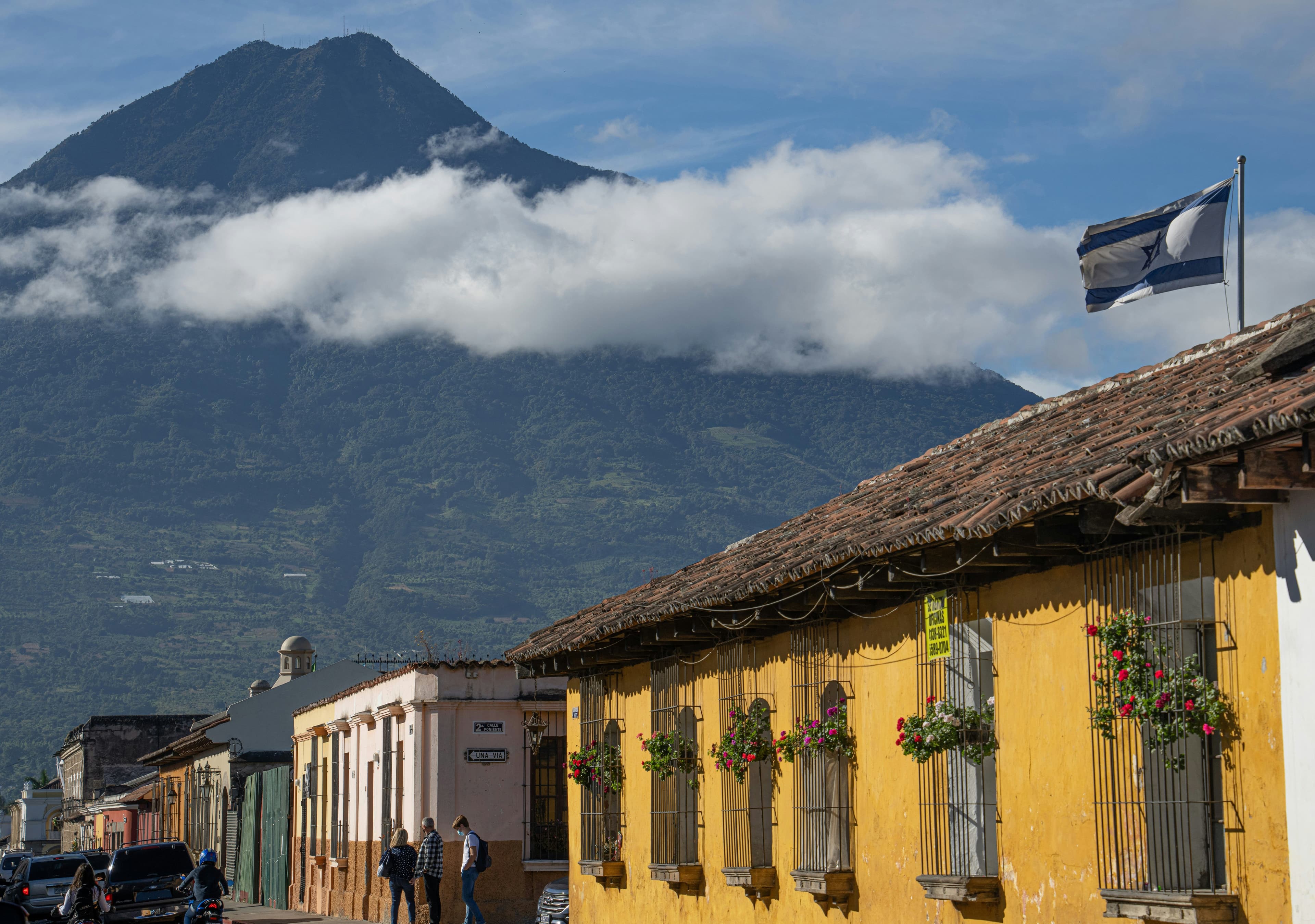 Colourful street in Guatemala with colonial buildings and a volcano in the background under a cloudy sky.