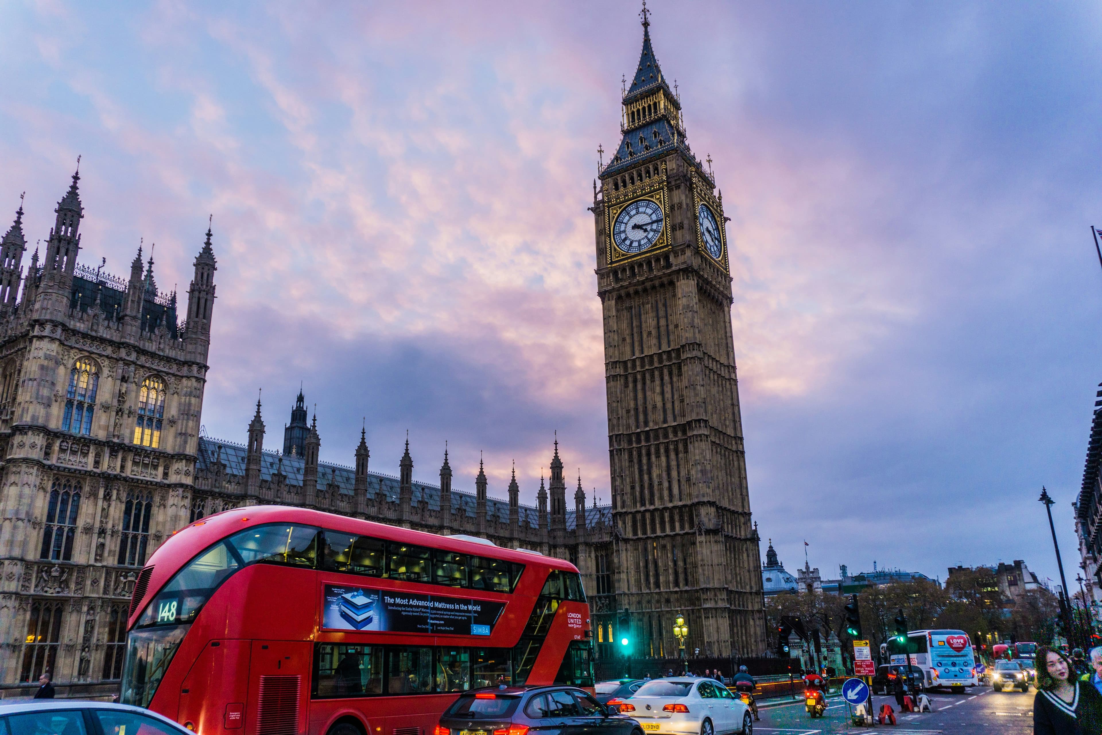 The big ben in london at sunset with a red hop-on-hop off bus in front of it