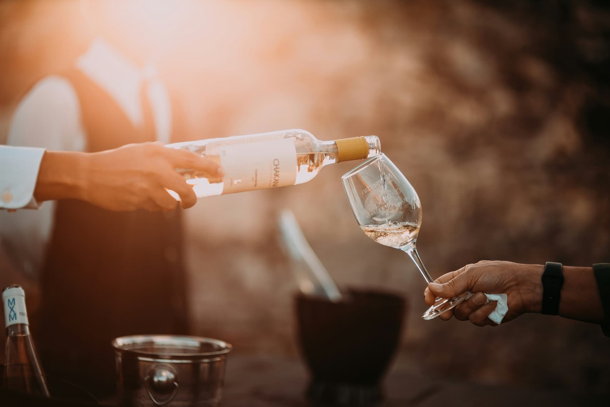 Waiter pouring wine from a bottle into a wine glass on a sunny day outside