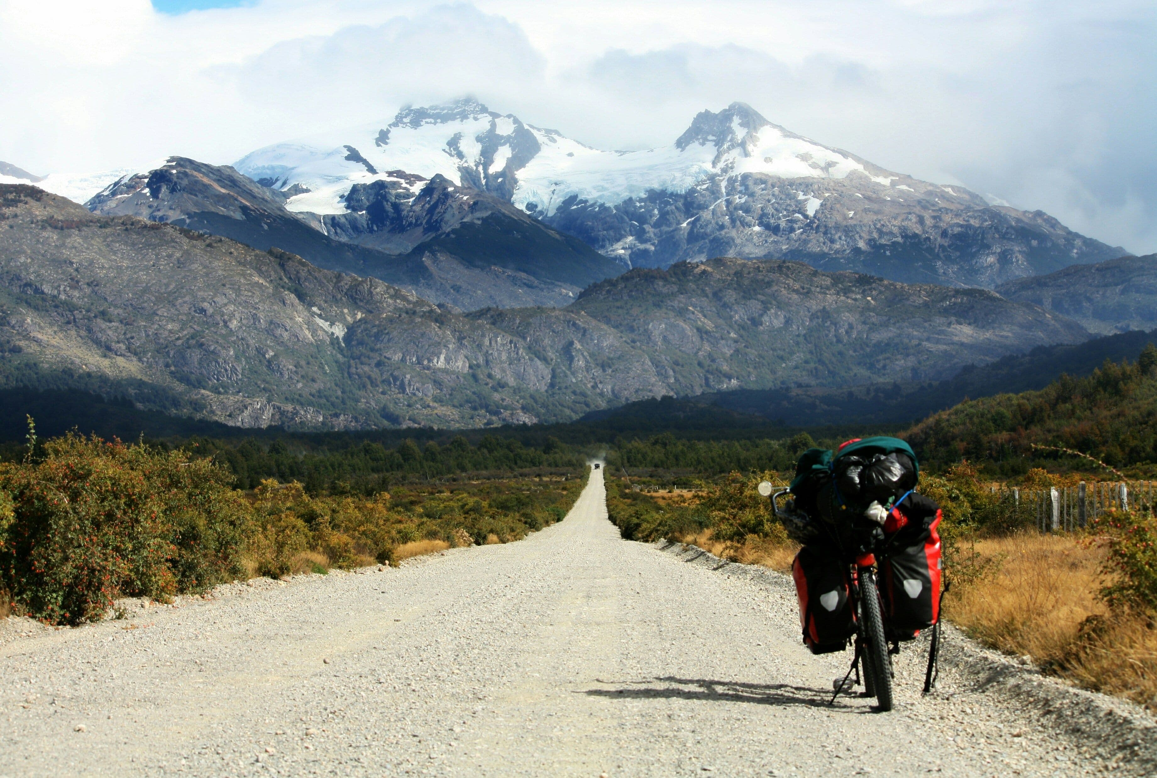 The road of Carretera Austral with a parked scooter on the right and mountain peaks in the background