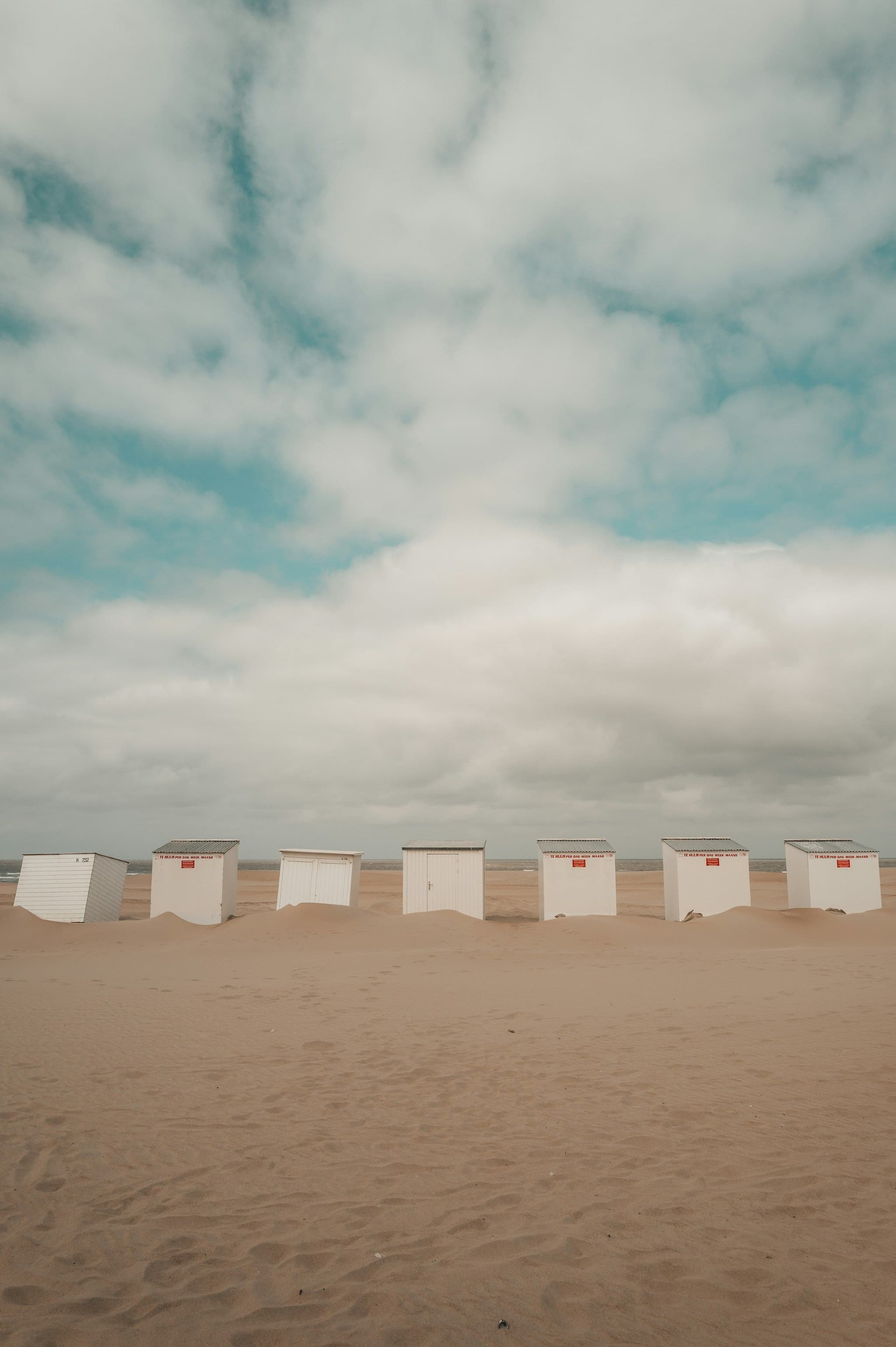 Beach huts lining a wide sandy shore under a cloudy sky