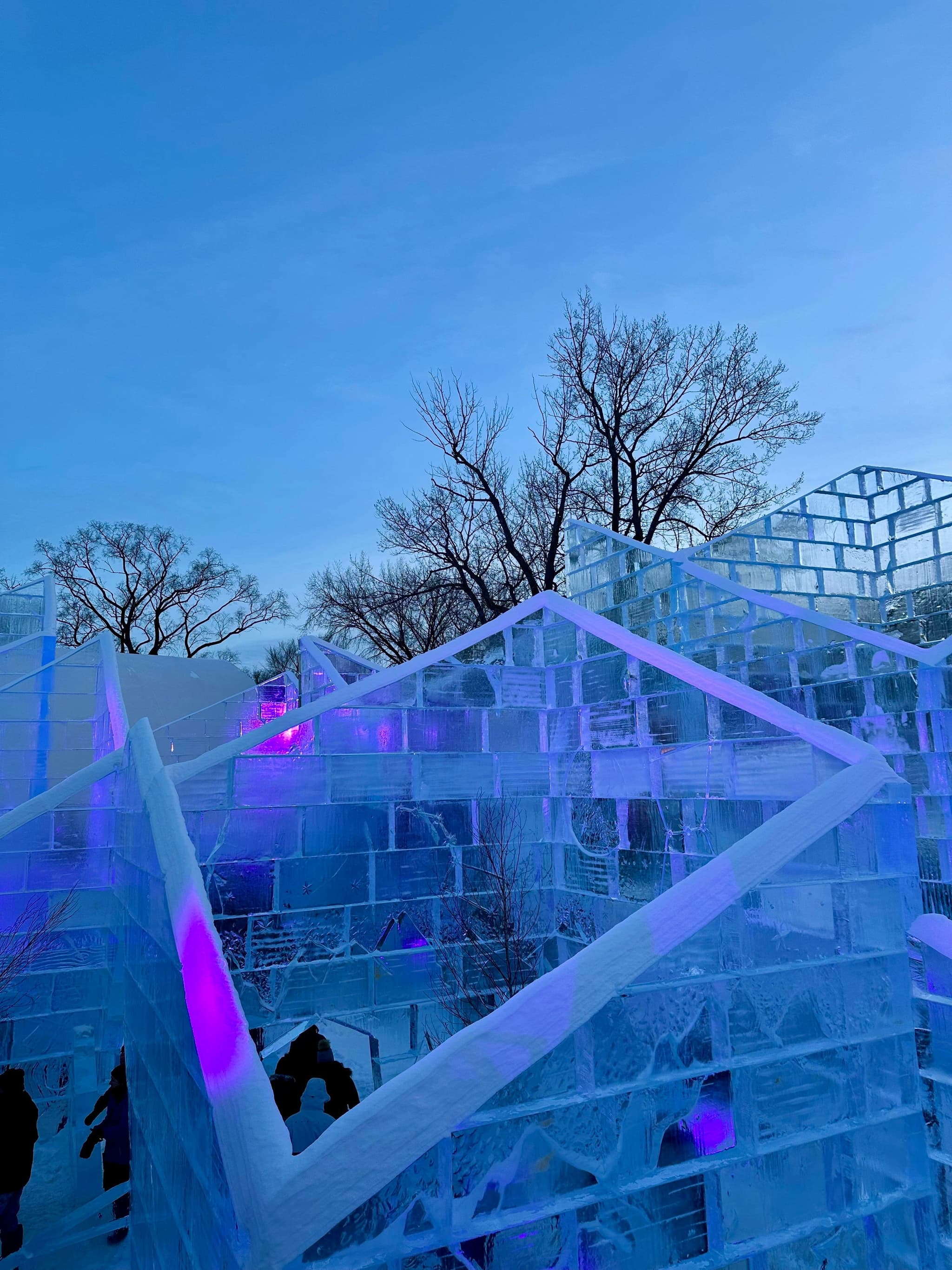 An illuminated ice castle glows at twilight, similar in spirit to the carnival's own Ice Palace, rebuilt from scratch with a new design every winter.
