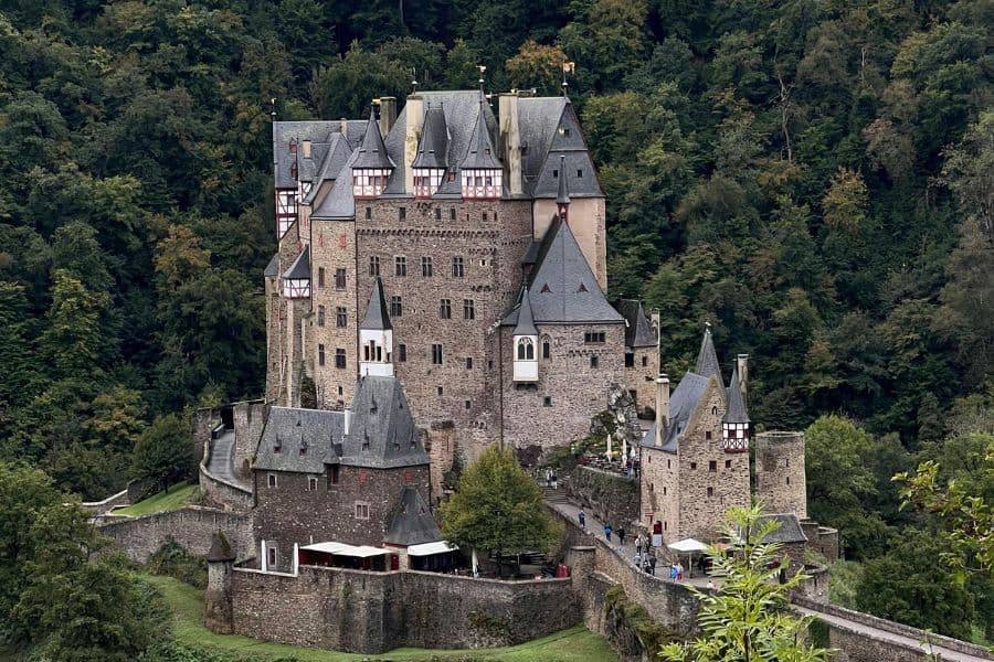 A stunning view of Burg Eltz rising out of the green forest against a clear blue sky.