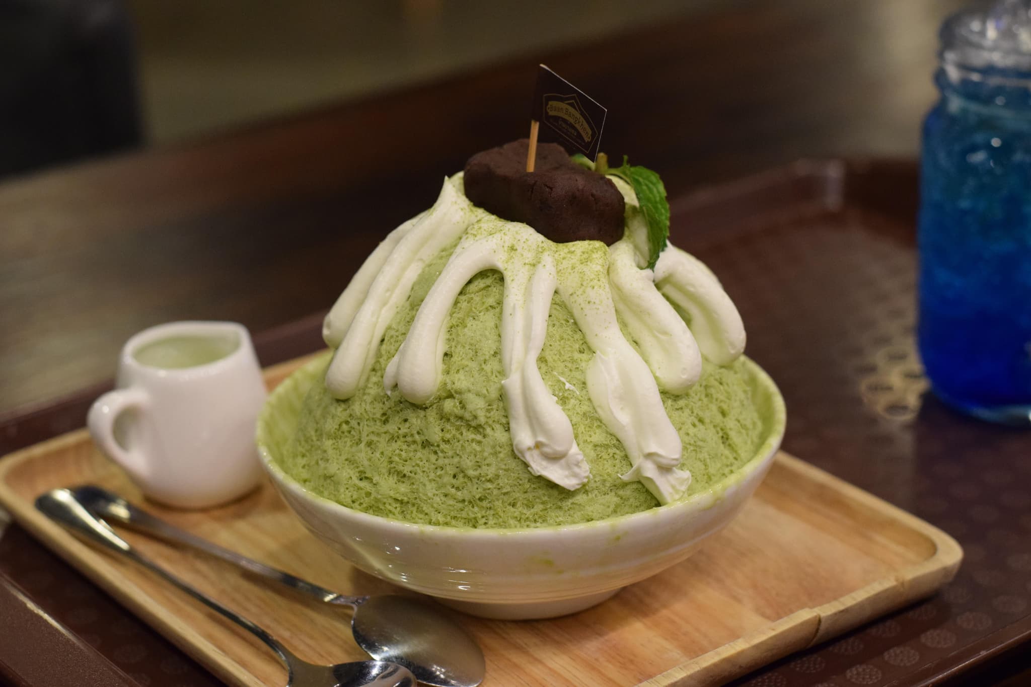 Green green tea Bingsu shaved ice served in a white bowl next to a cup of coffee