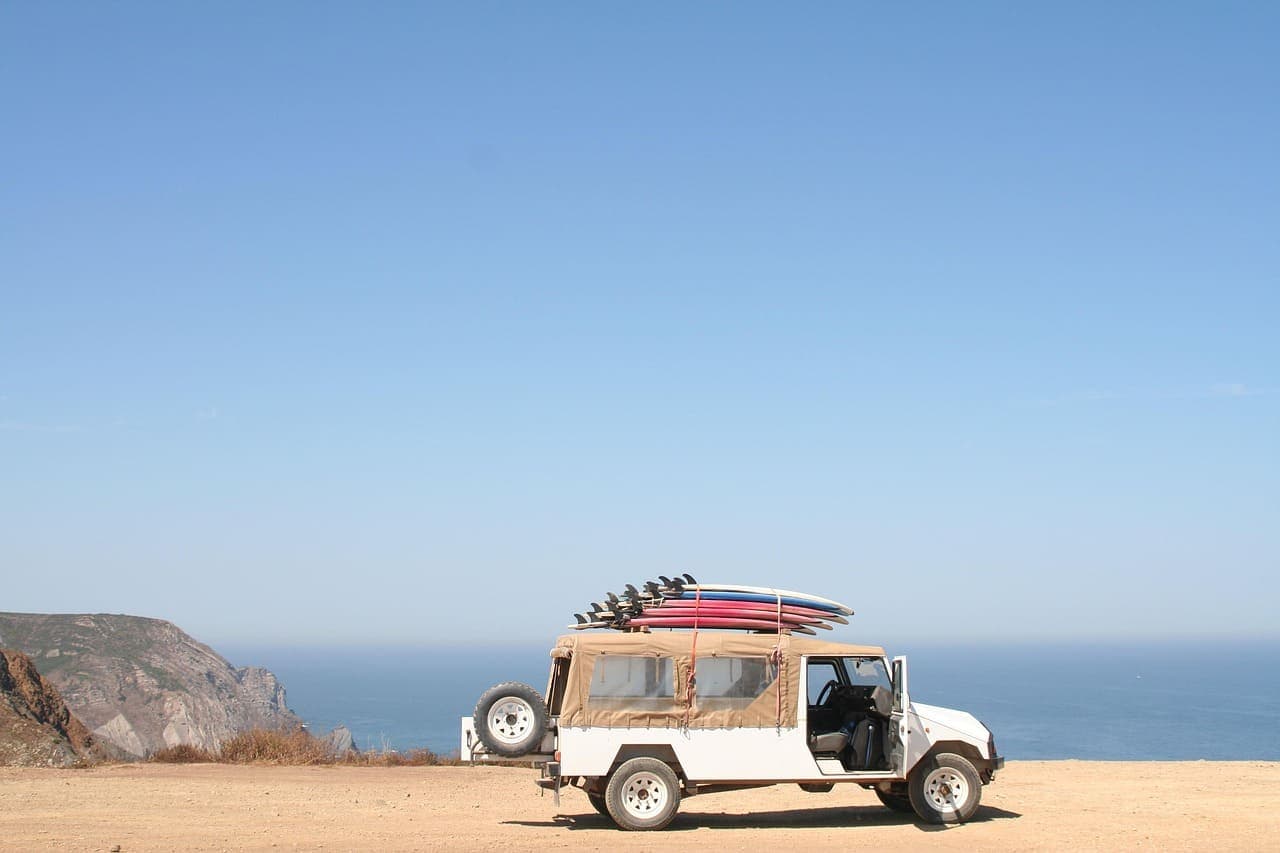 Off-road vehicle parked on a coastal cliff with surfboards on the roof and the ocean in the background.