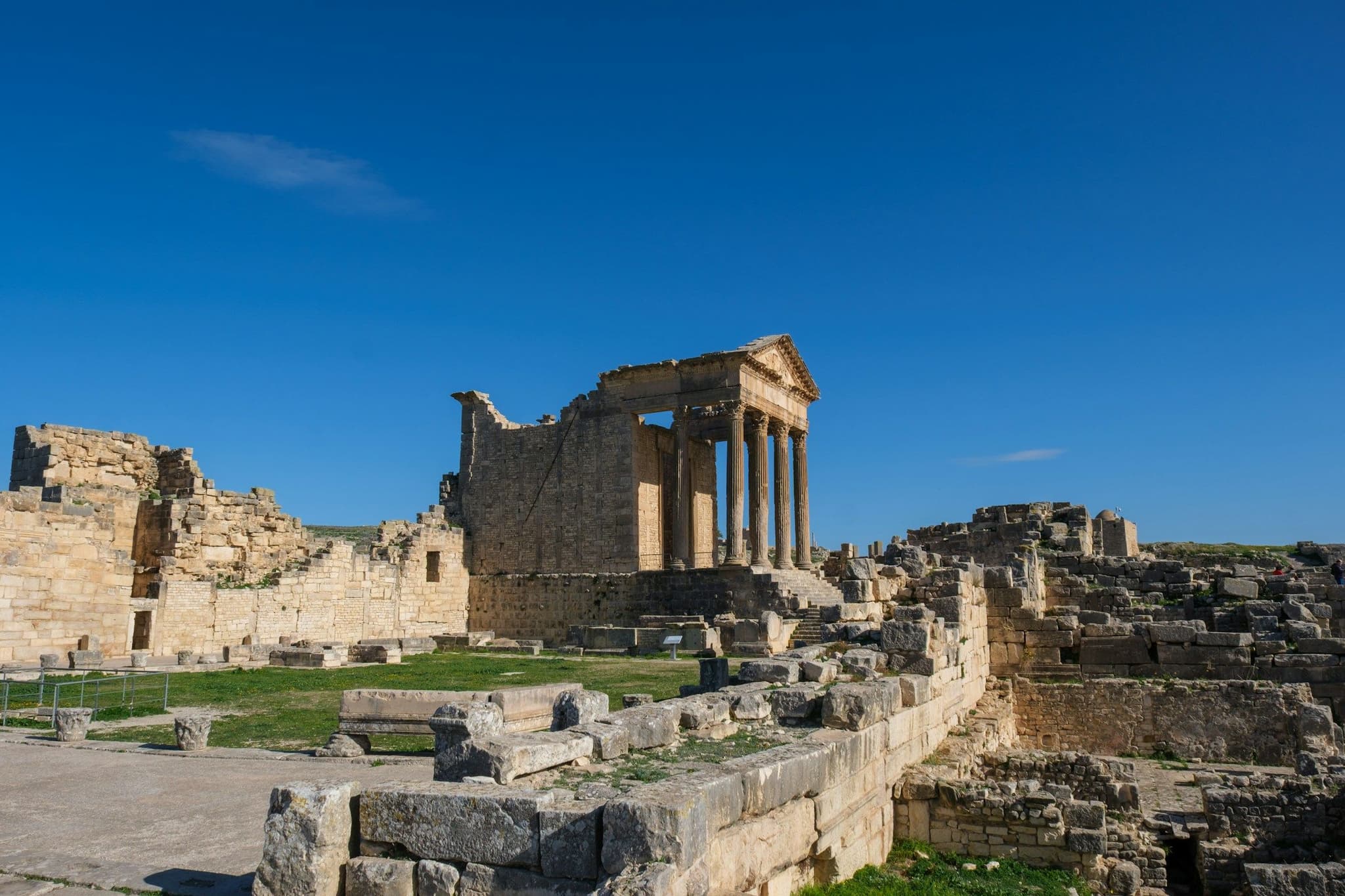 A partly standing Roman temple among ruins on a hillside