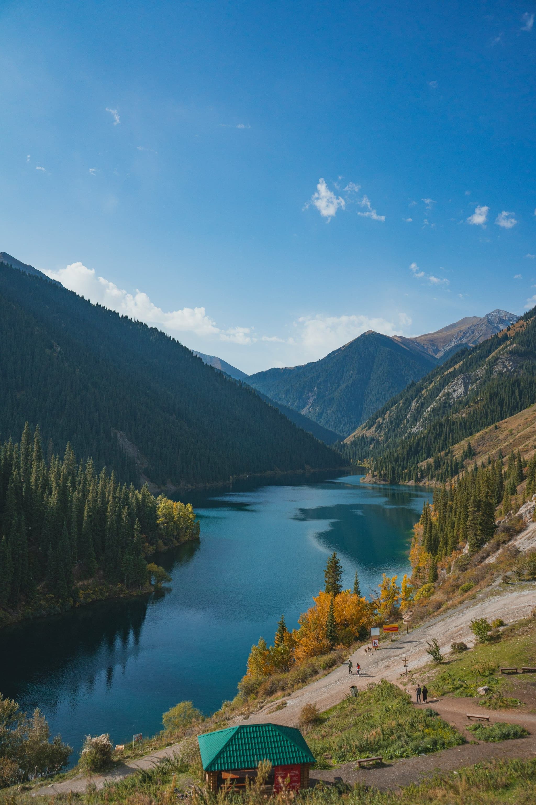 A forested mountain lake under a blue sky in the Kolsai area