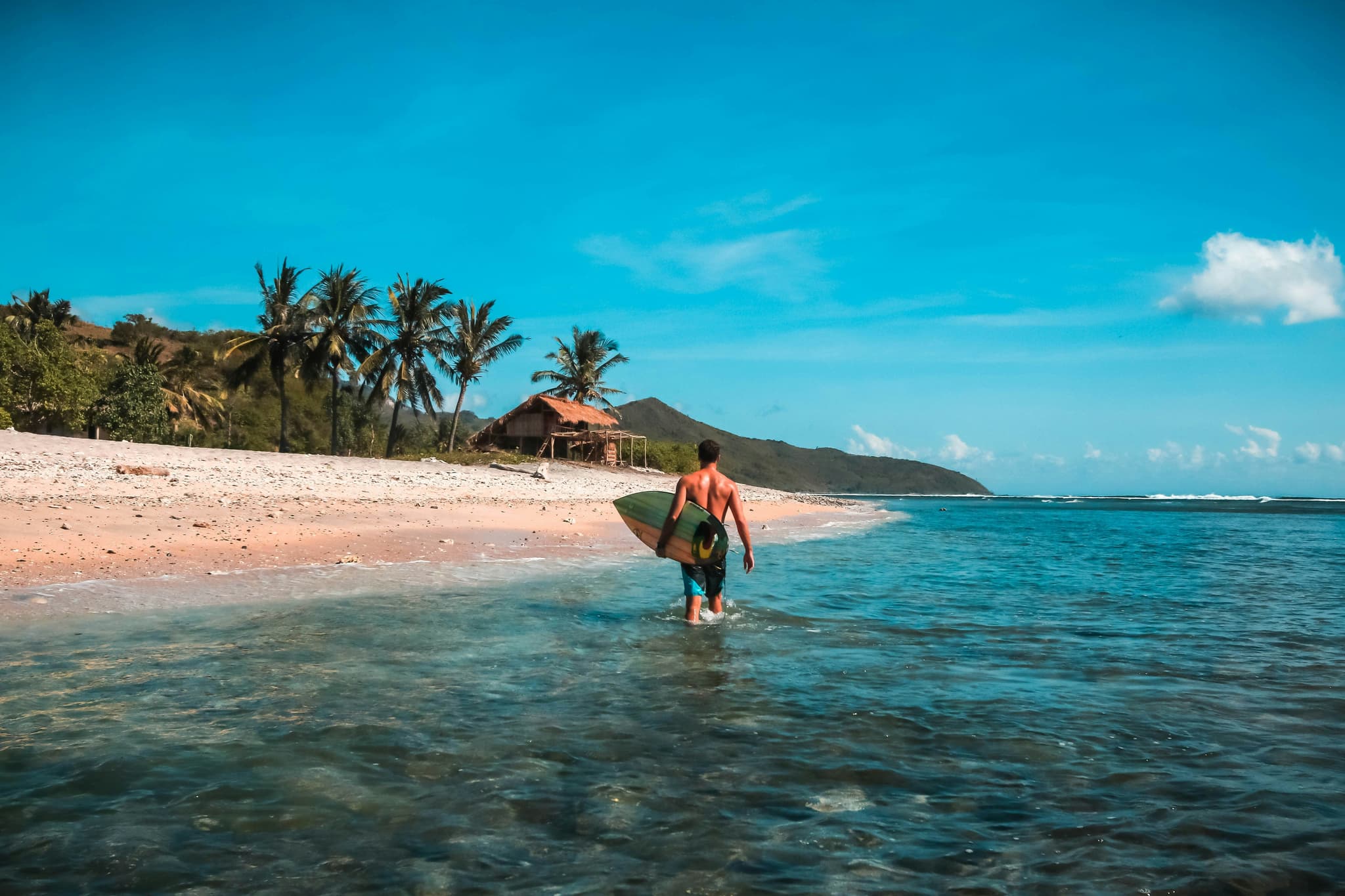 Surfer walking with surf board on lombok island in the sea next to empty beach