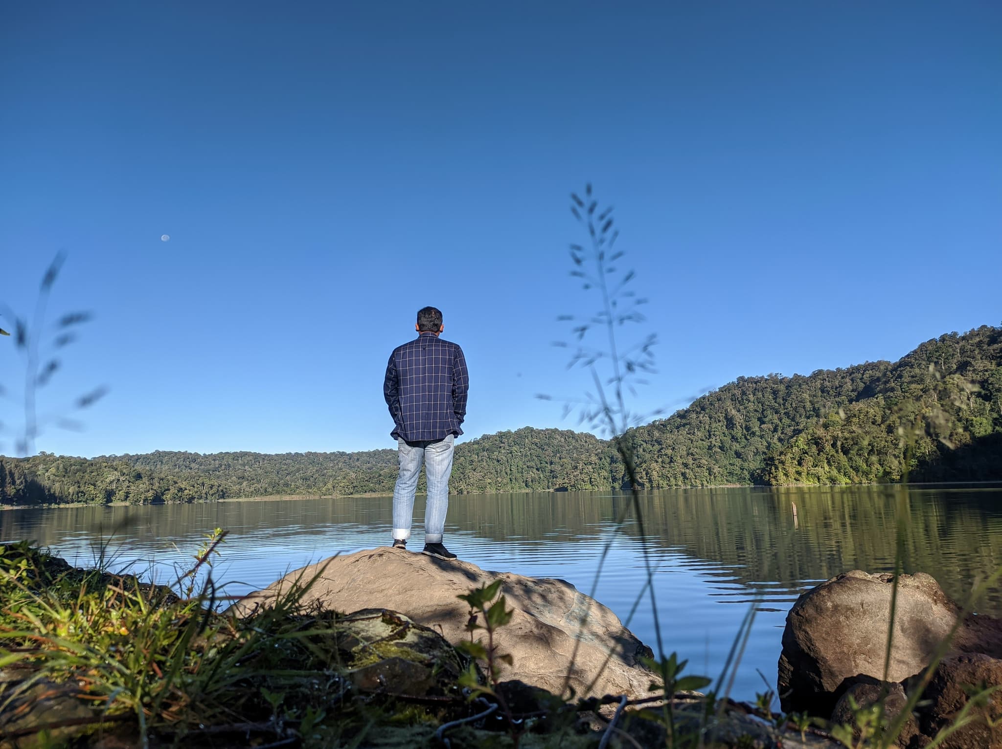 Solo traveller man standing on a rock looking at the lake and surrounding forest on a clear day