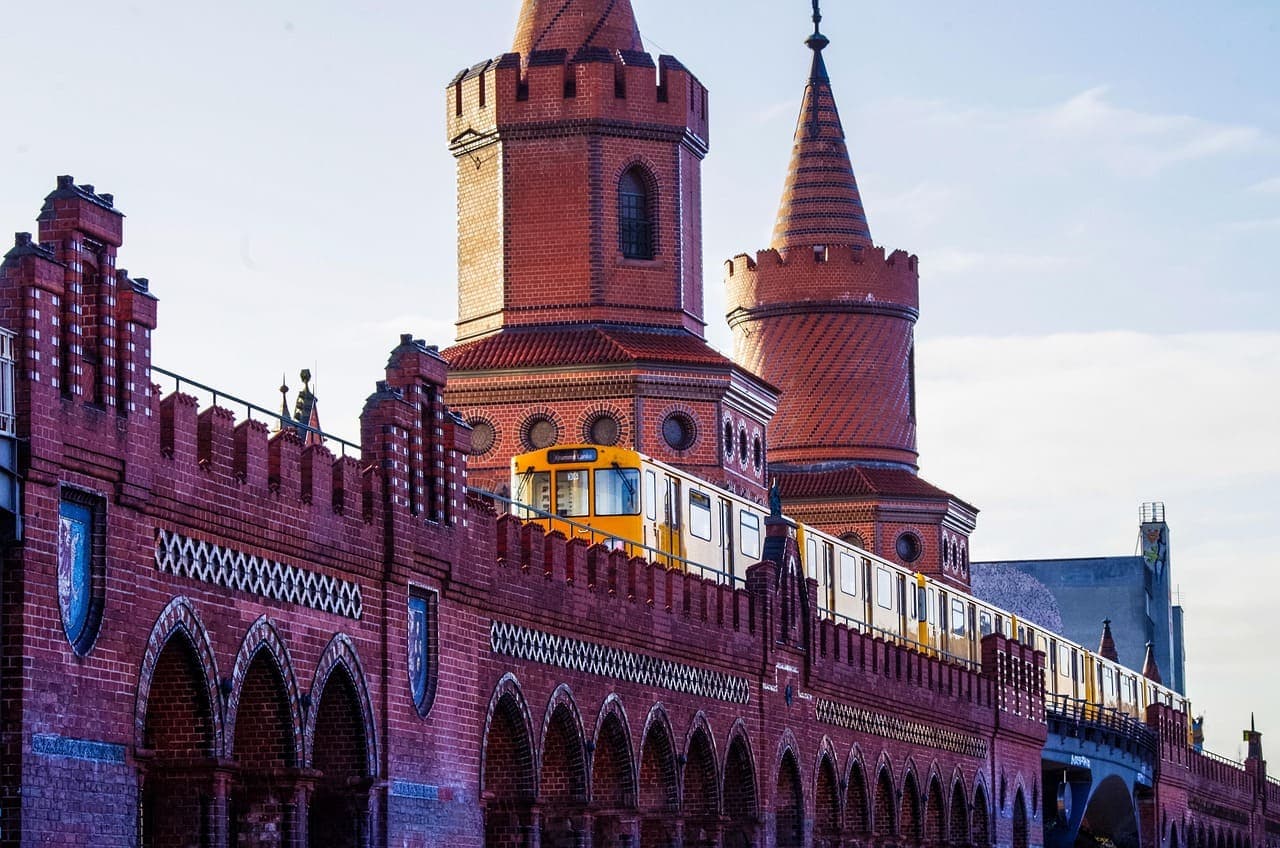 A yellow train crossing the red brick Oberbaum Bridge in Berlin at sunset, with historic towers in the background.
