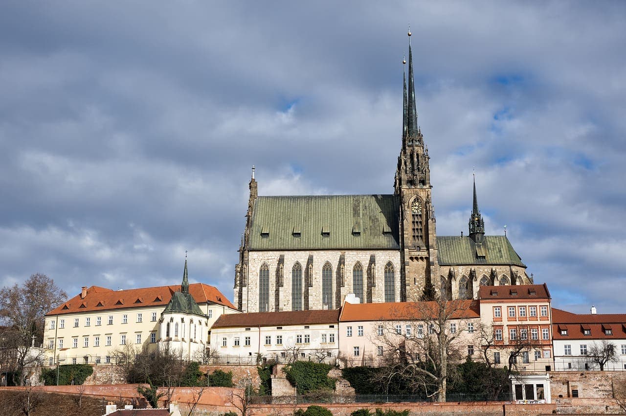 St. Barbara’s Church in Kutná Hora standing on a hill with dramatic Gothic architecture and cloudy skies behind it.