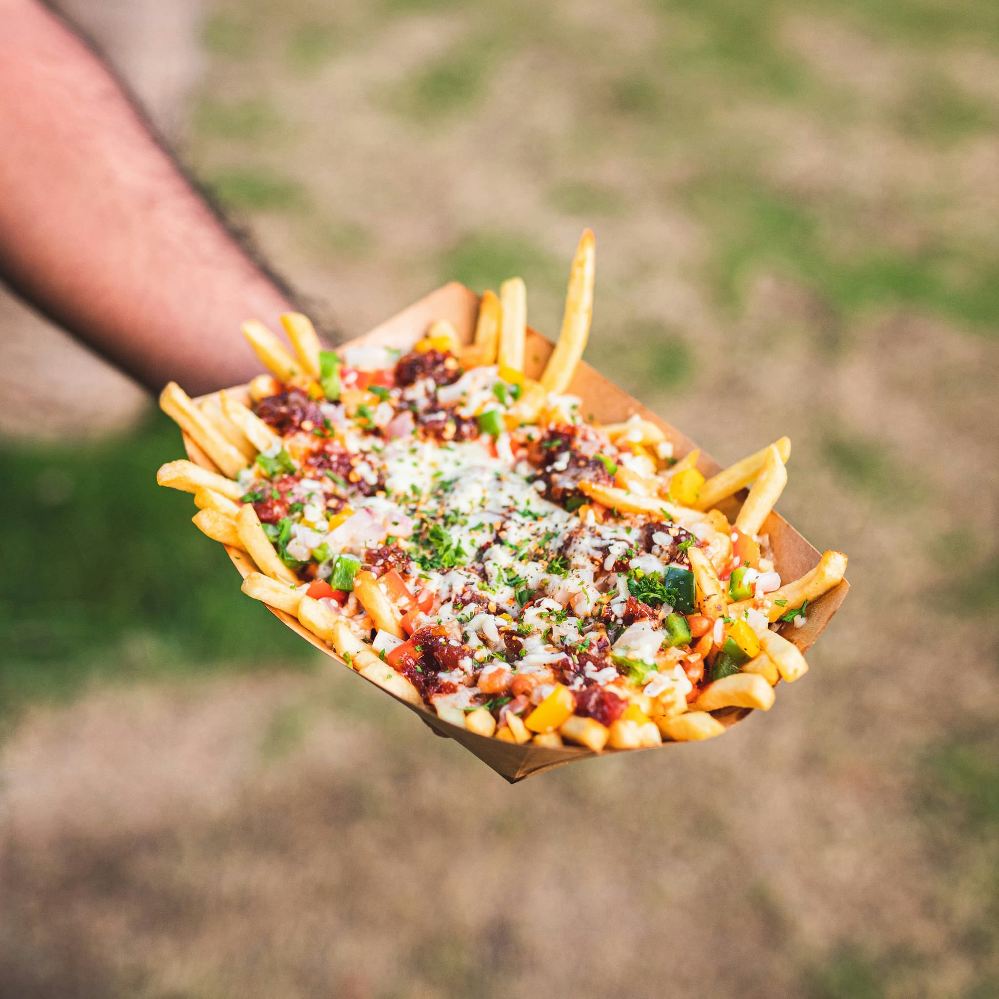 A hand holding a paper box of poutine with fries