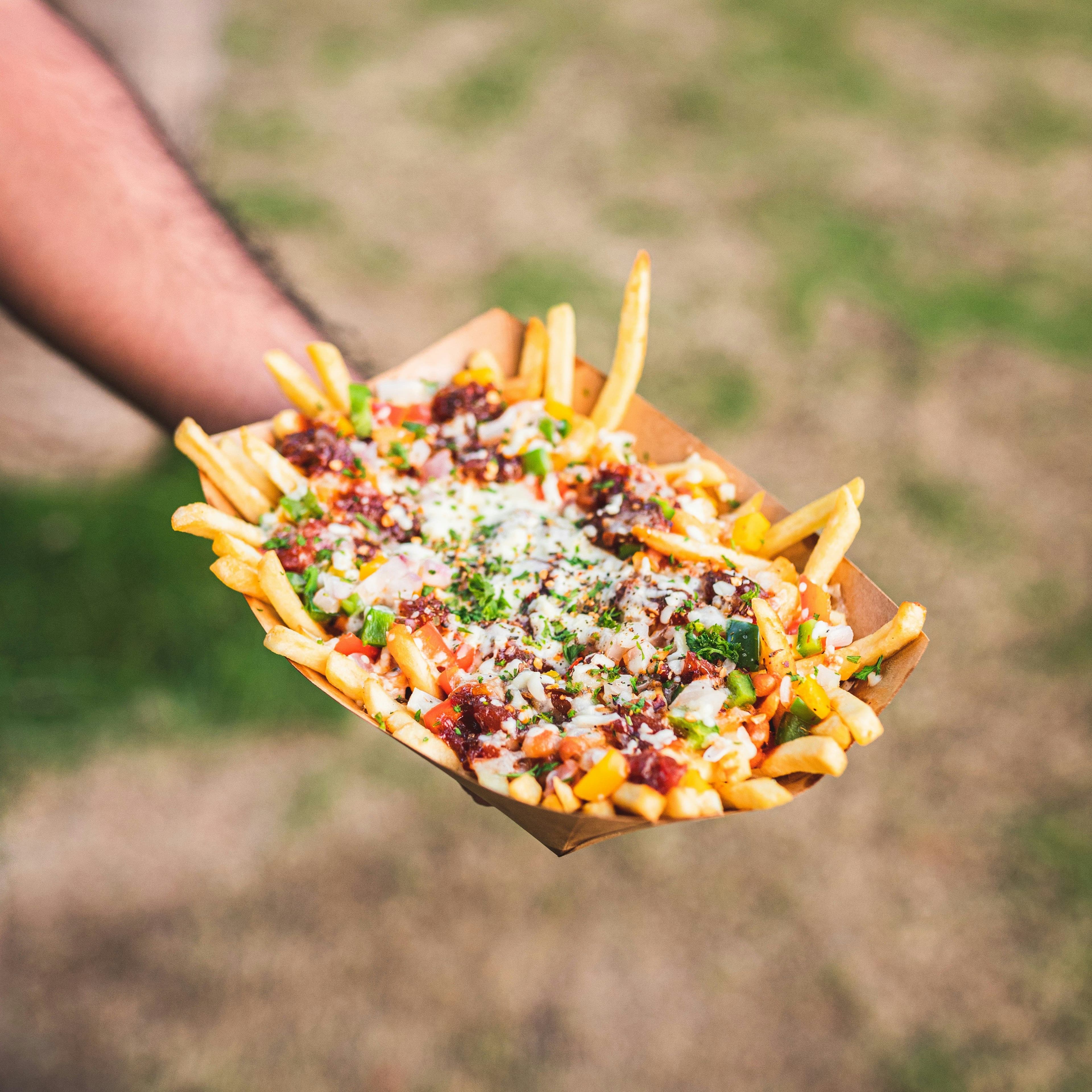 A hand holding a paper box of poutine with fries