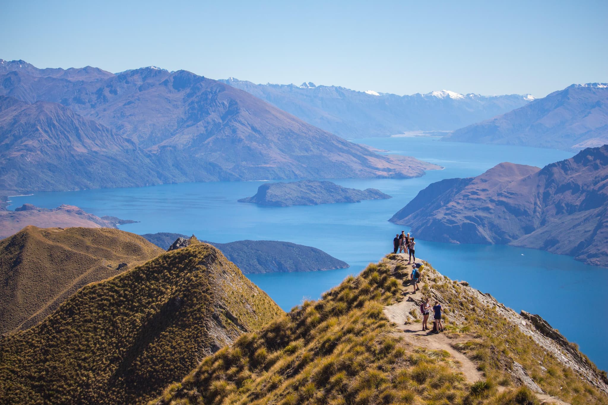 hikers standing on Roy's Peak green mountain surrounded by lake