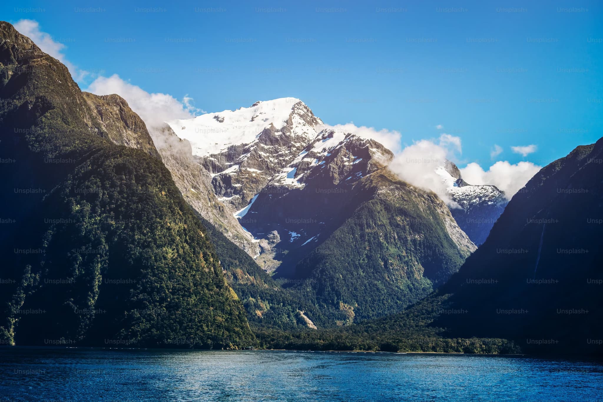 Majestic snow-capped mountain surrounded by lush green peaks, under a clear blue sky, reflected in a serene body of water, evoking tranquility.
