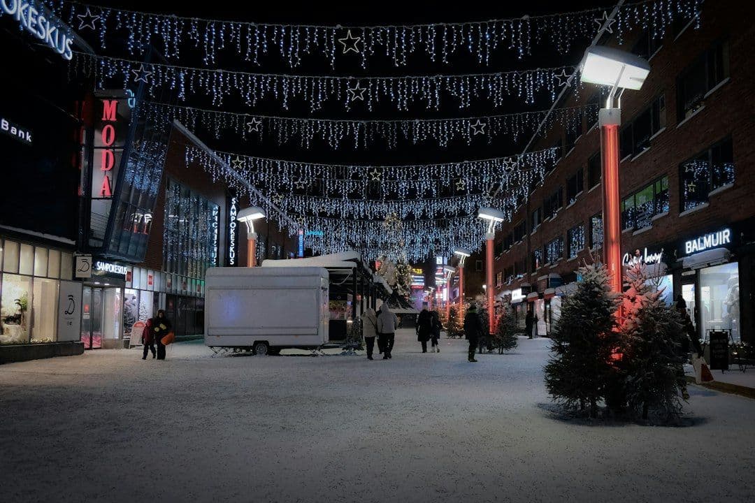 A snowy evening in Rovaniemi's Sampokeskus district, decorated with festive lights and busy with visitors.